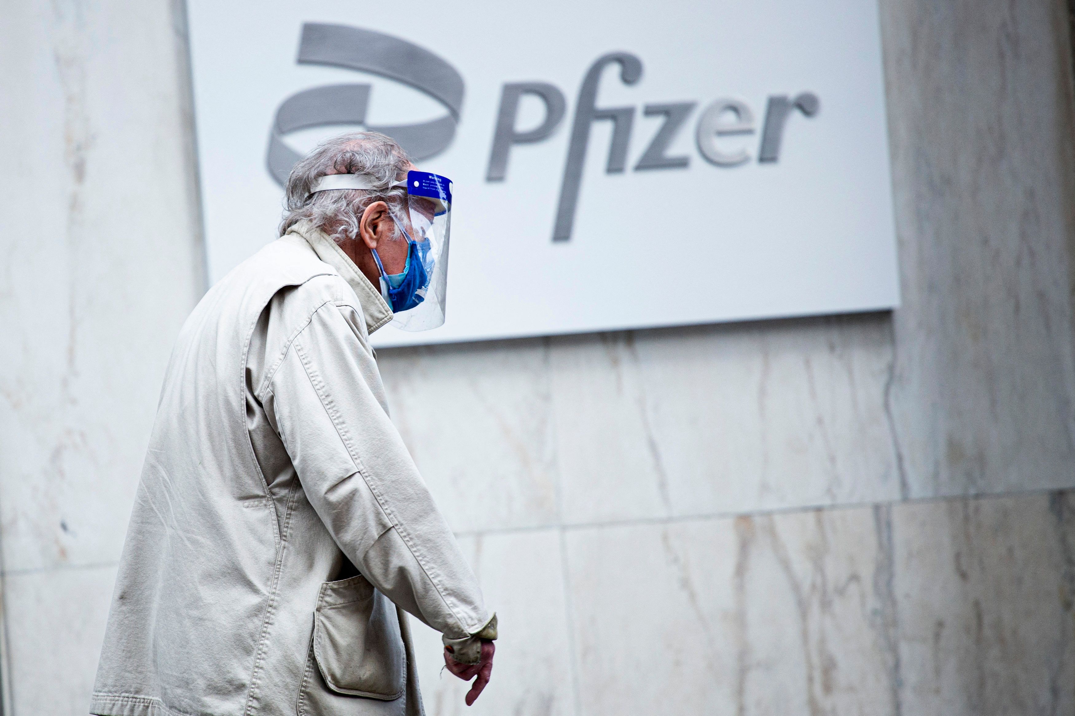 Seorang warga mengenakan masker dan facemask melintas di depan logo Pfizer di New York, AS.
