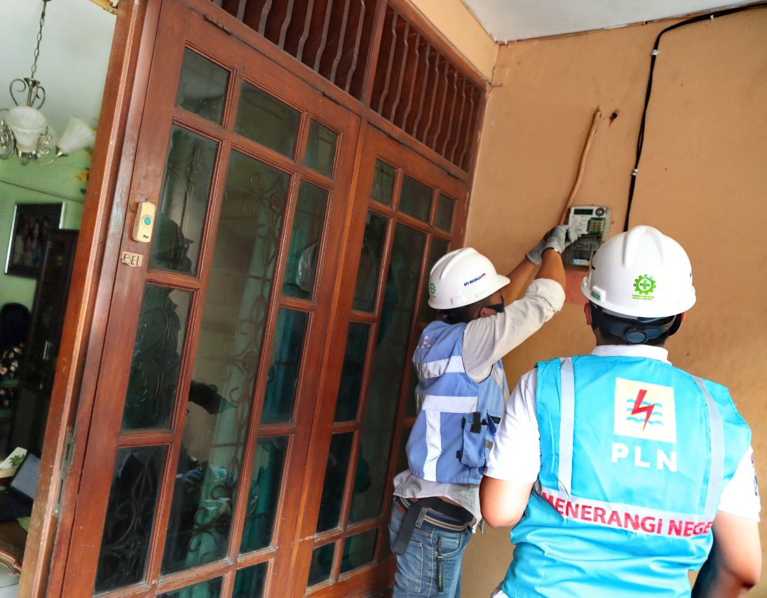 Ilustrasi petugas PLN melakukan penambahan daya di kWh meter rumah pelanggan.