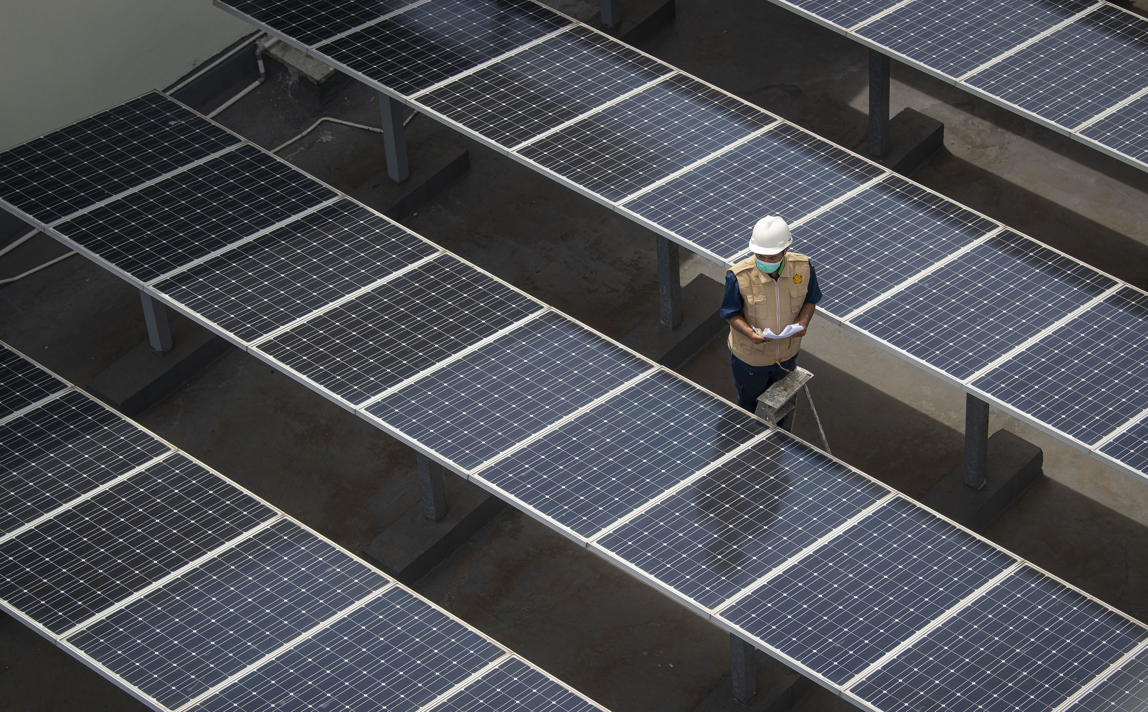 Petugas membersihkan atap panel surya yang terpasang di atas gedung Dirjen Ketenagalistrikan kementerian ESDM