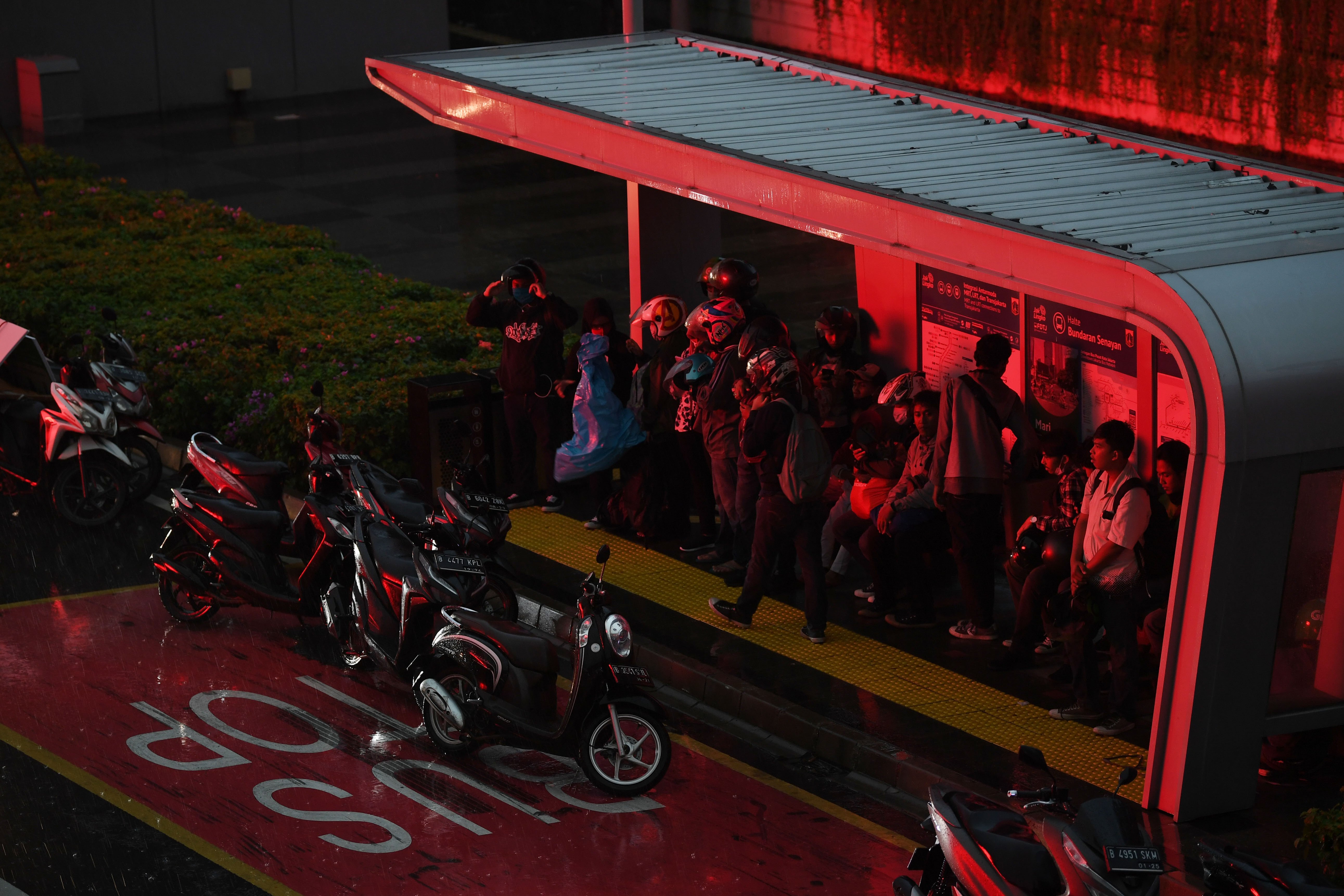 Pengendara sepeda motor berteduh di seuah halte saat hujan