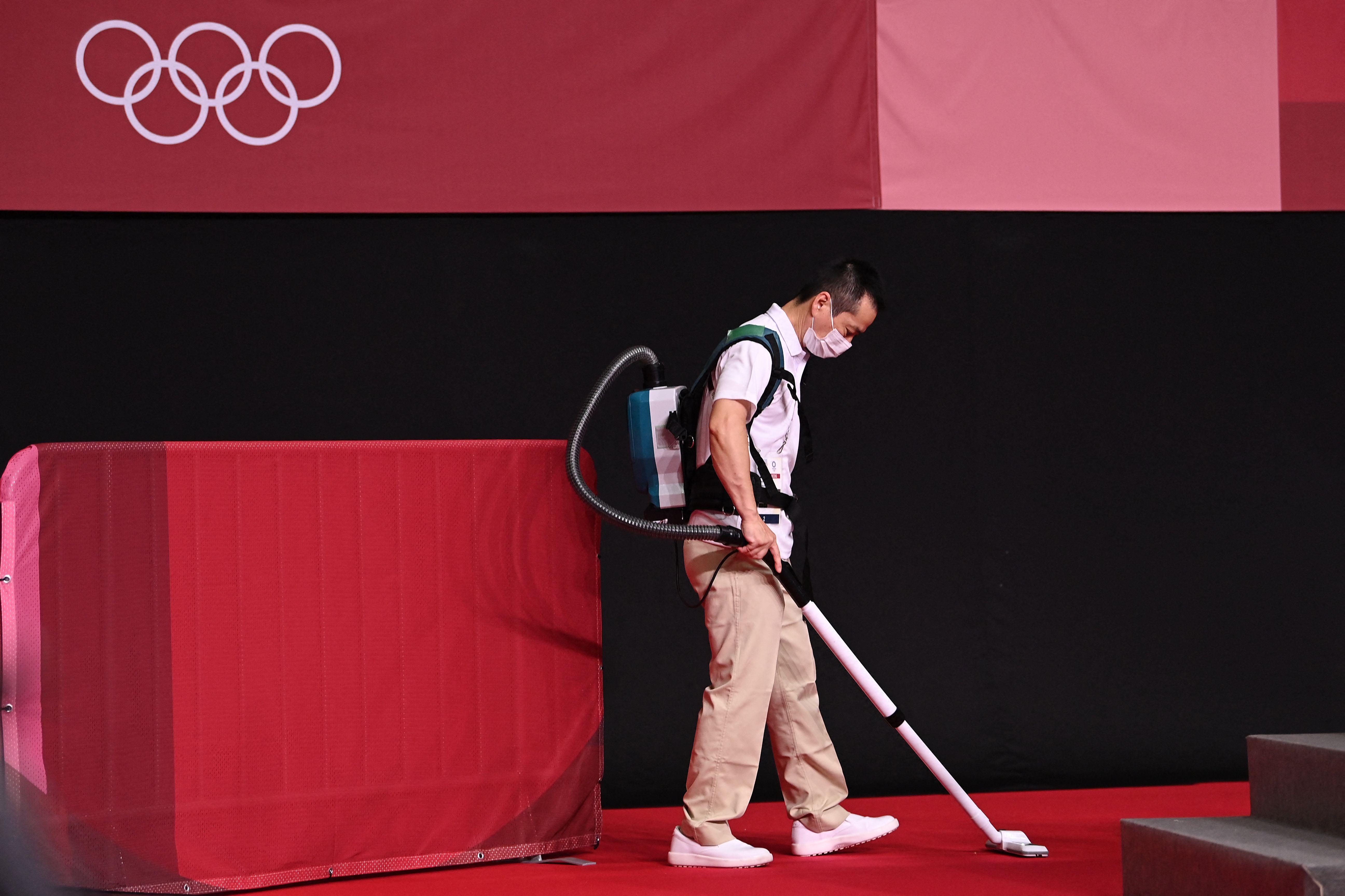 Seorang pekerja tengah membersihan karpet dengan vacuum cleaner di Olimpiade Tokyo 2020.