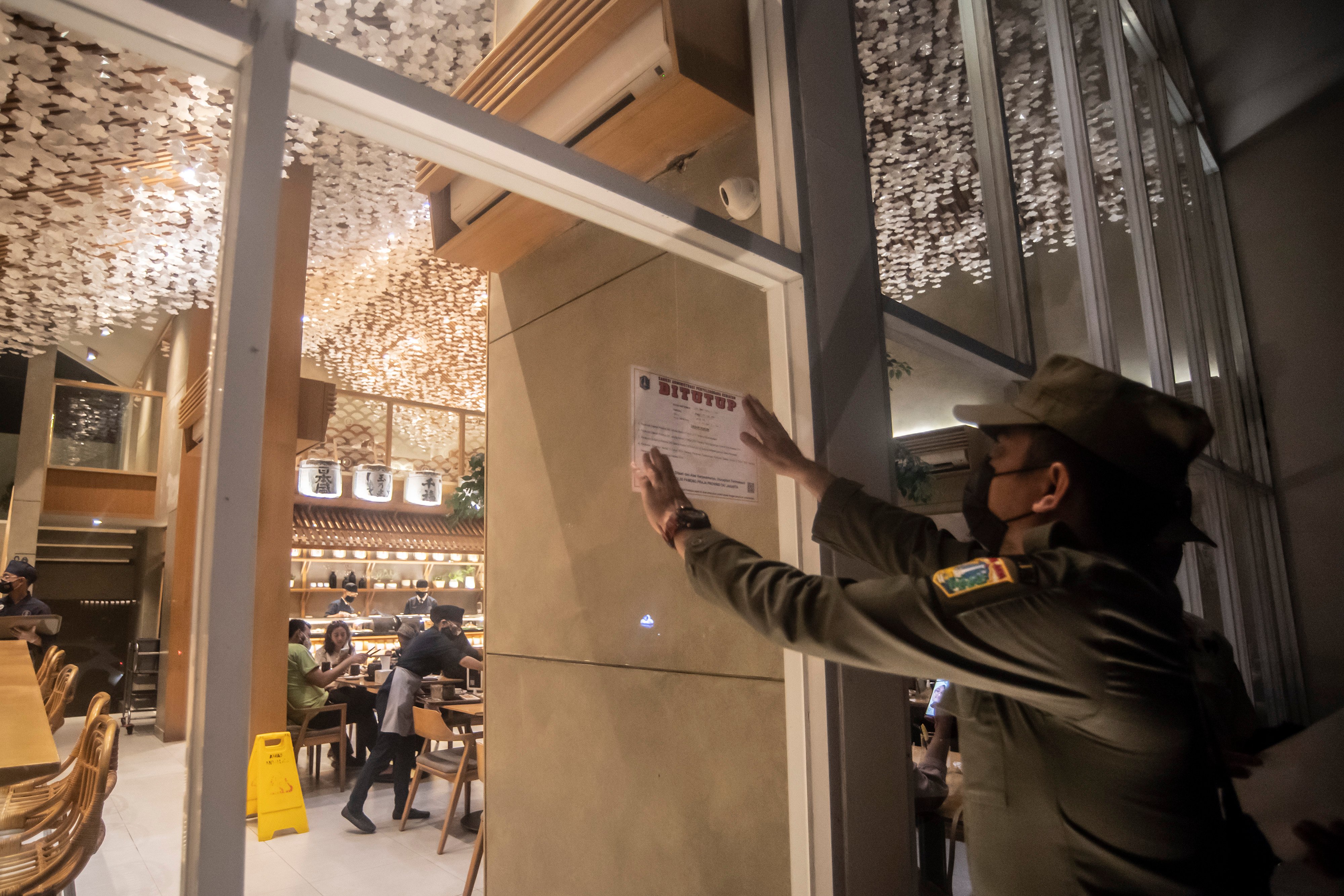 Petugas menempelkan stiker sanksi pada kafe yang melanggar aturan PPKM level 3 di Jakarta Selatan.