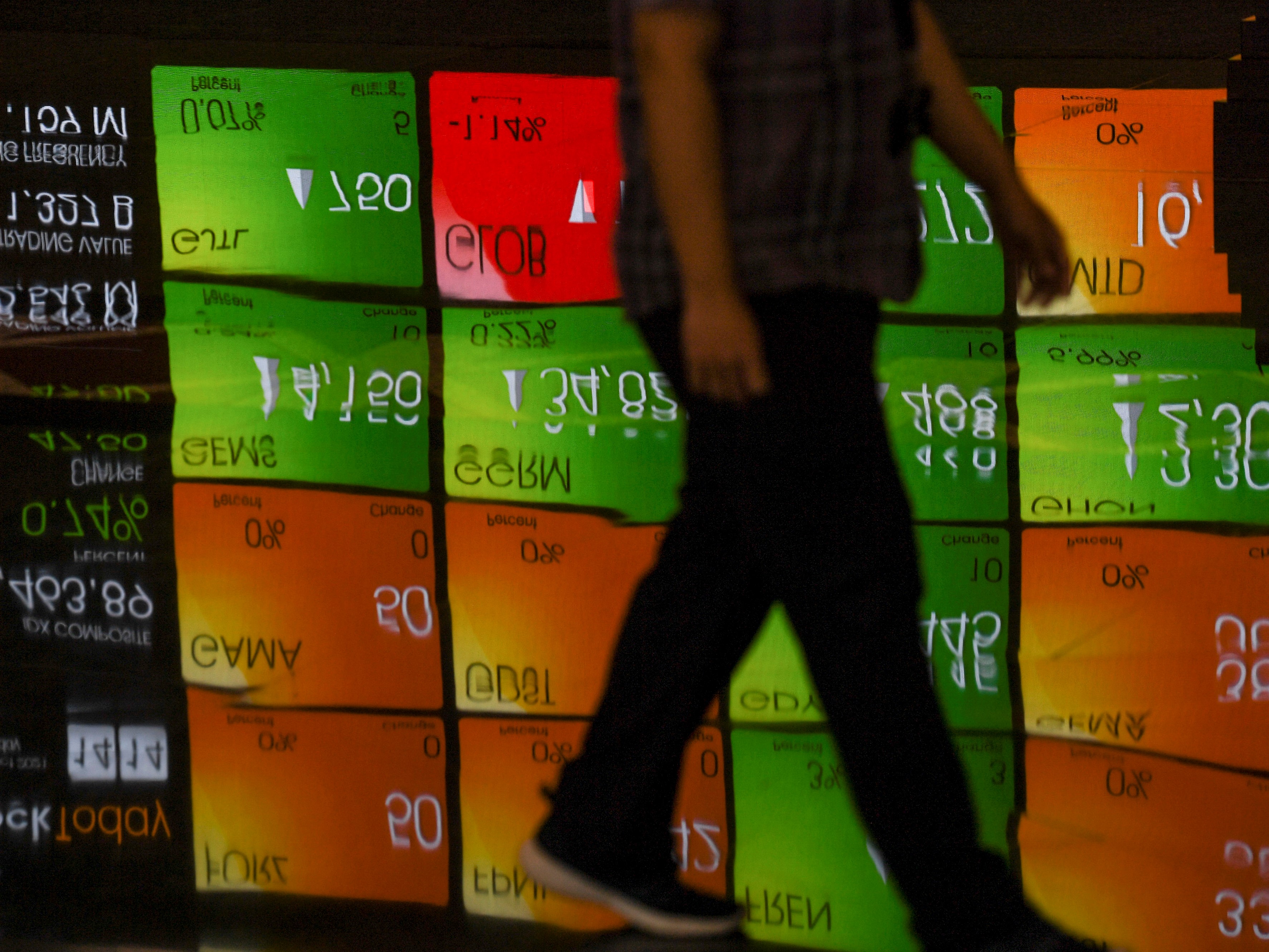 Karyawan melintas di dekat layar yang menampilkan pergerakan saham di Bursa Efek Indonesia, Jakarta.