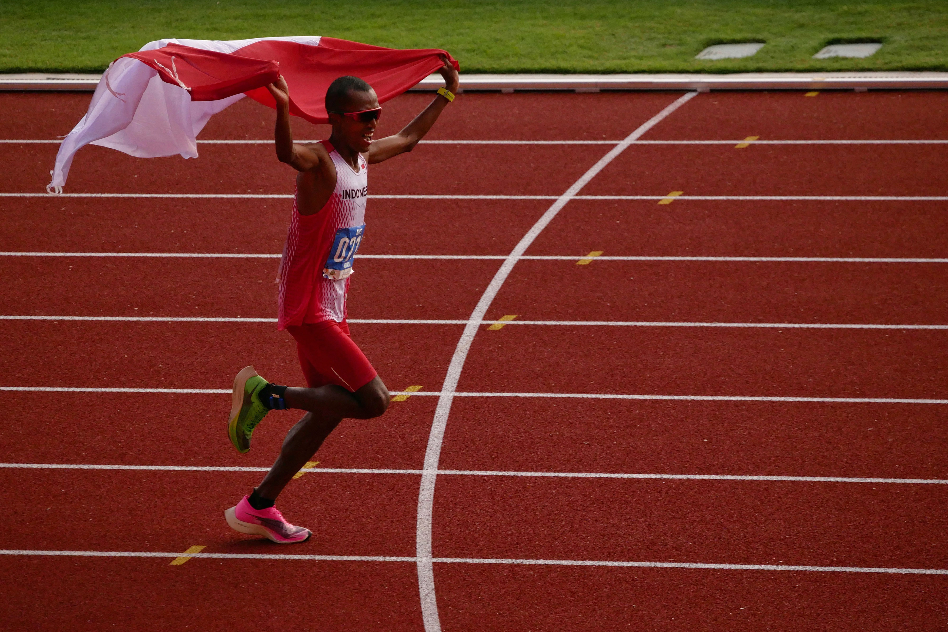 Pelari Indonesia Agus Prayogo mengibarkan bendera Merah Putih saat memasuki garis finish nomor marathon putra SEA Games 2019.