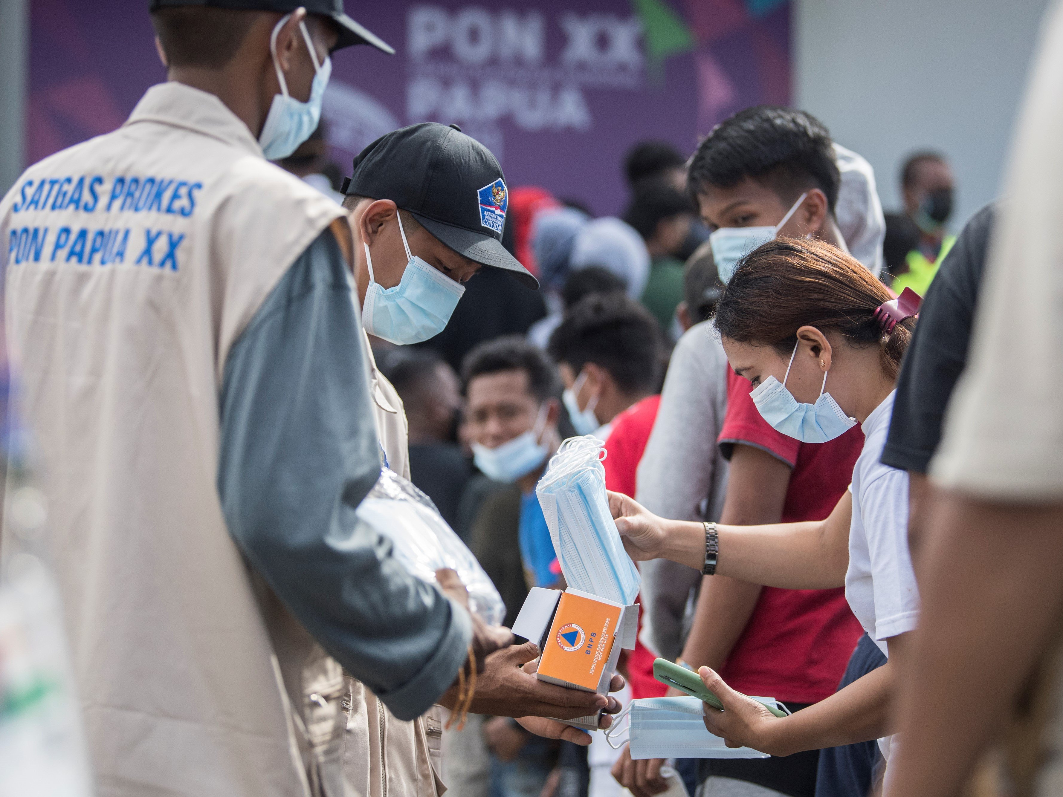 Satgas Prokes membagikan masker kepada warga yang mengantre untuk masuk menyaksikan pertandingan cabang olahraga futsal PON XX Papua.