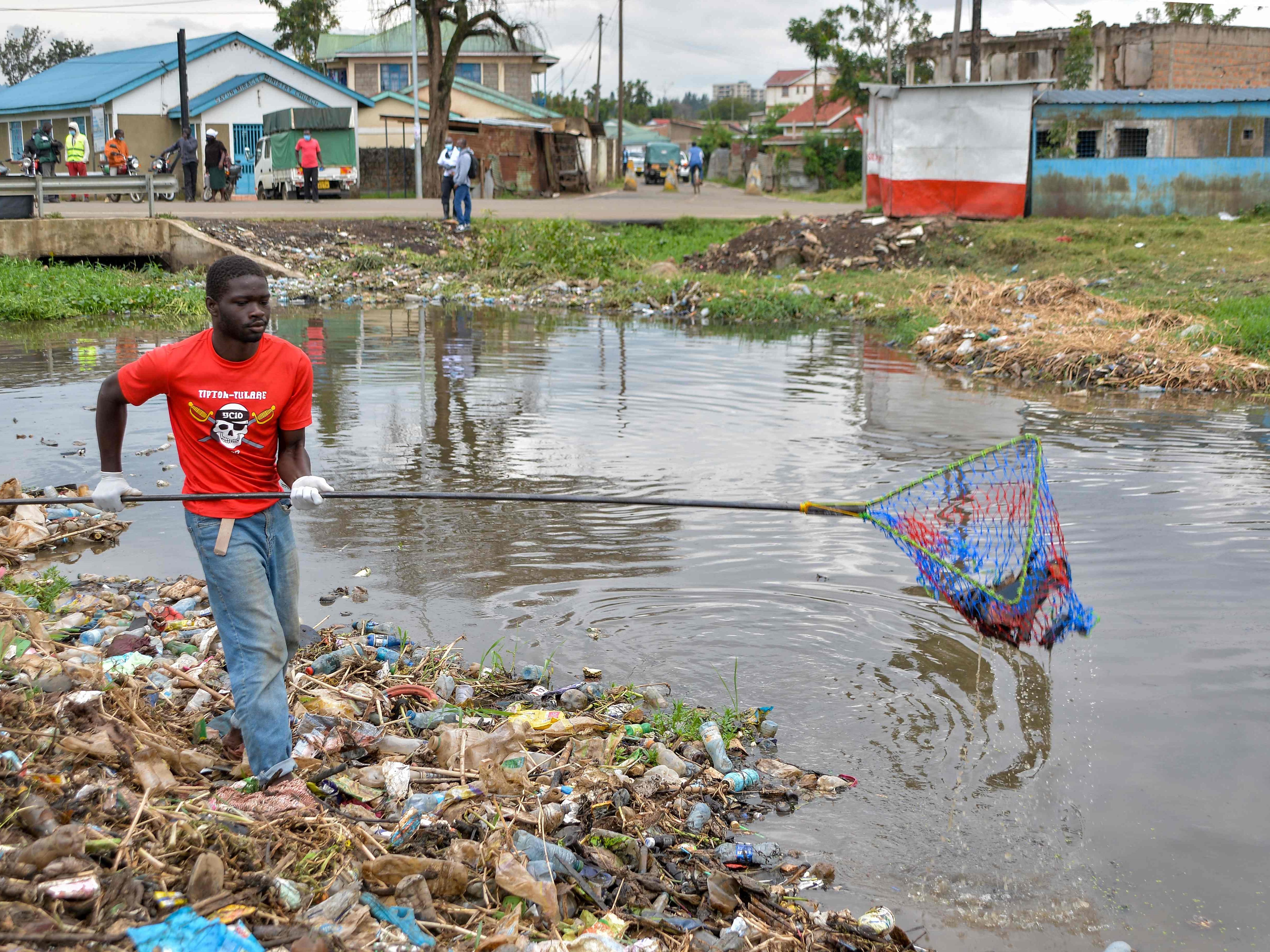 Seorang sukarelawan membersihkan dengan jaring sejumlah plastik dan sampah padat lain dari Sungai Wigwa di Kisumu, Kenya barat.