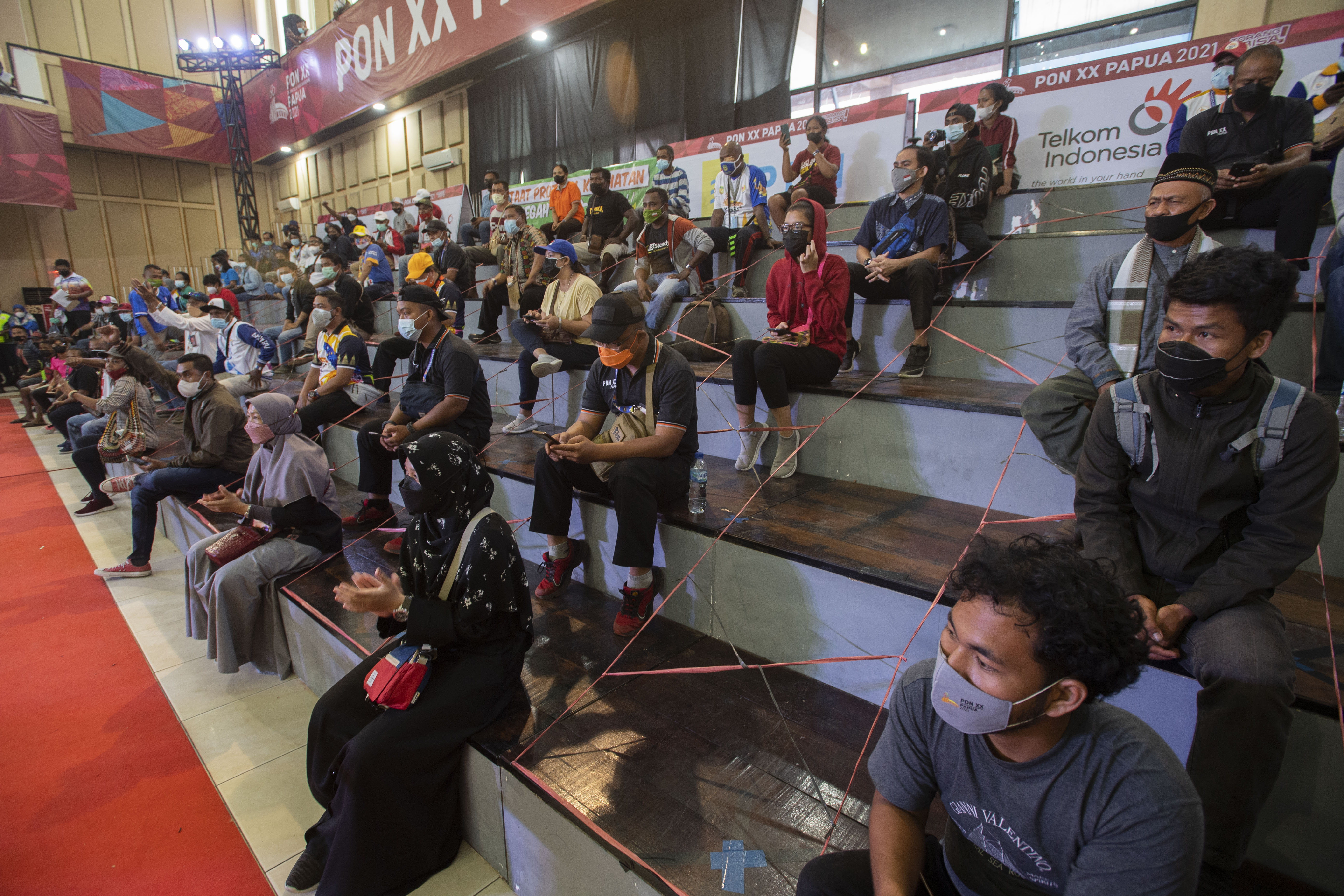 Penonton duduk dengan menjaga jarak menyaksikan tarung derajat PON Papua di Gedung Eme Neme Yauware, Mimika, Papua, Jumat (8/20/2021).