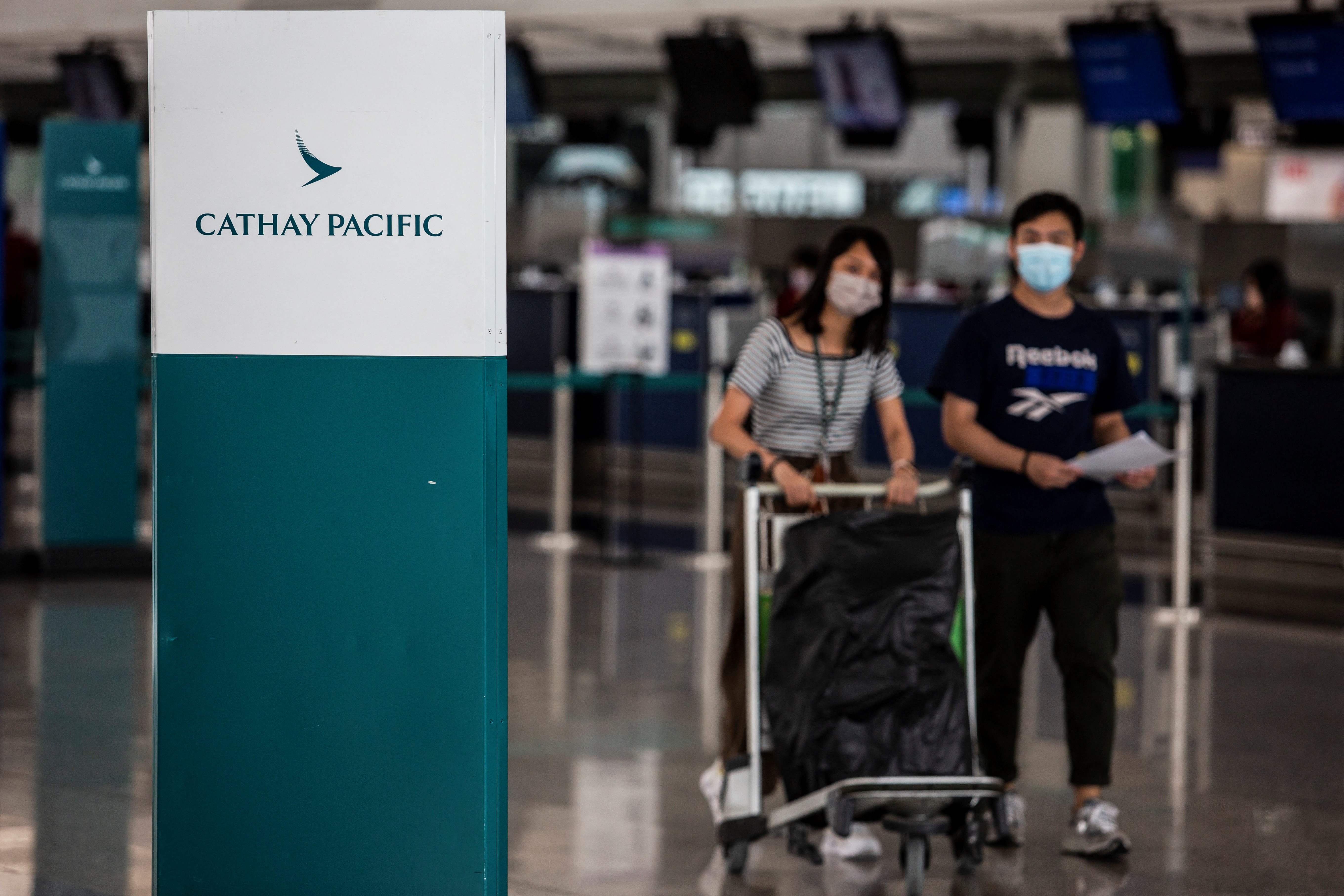Penumpang pesawat melintasi logo Cathay Pacific di Bandara Internasional Hong Kong.