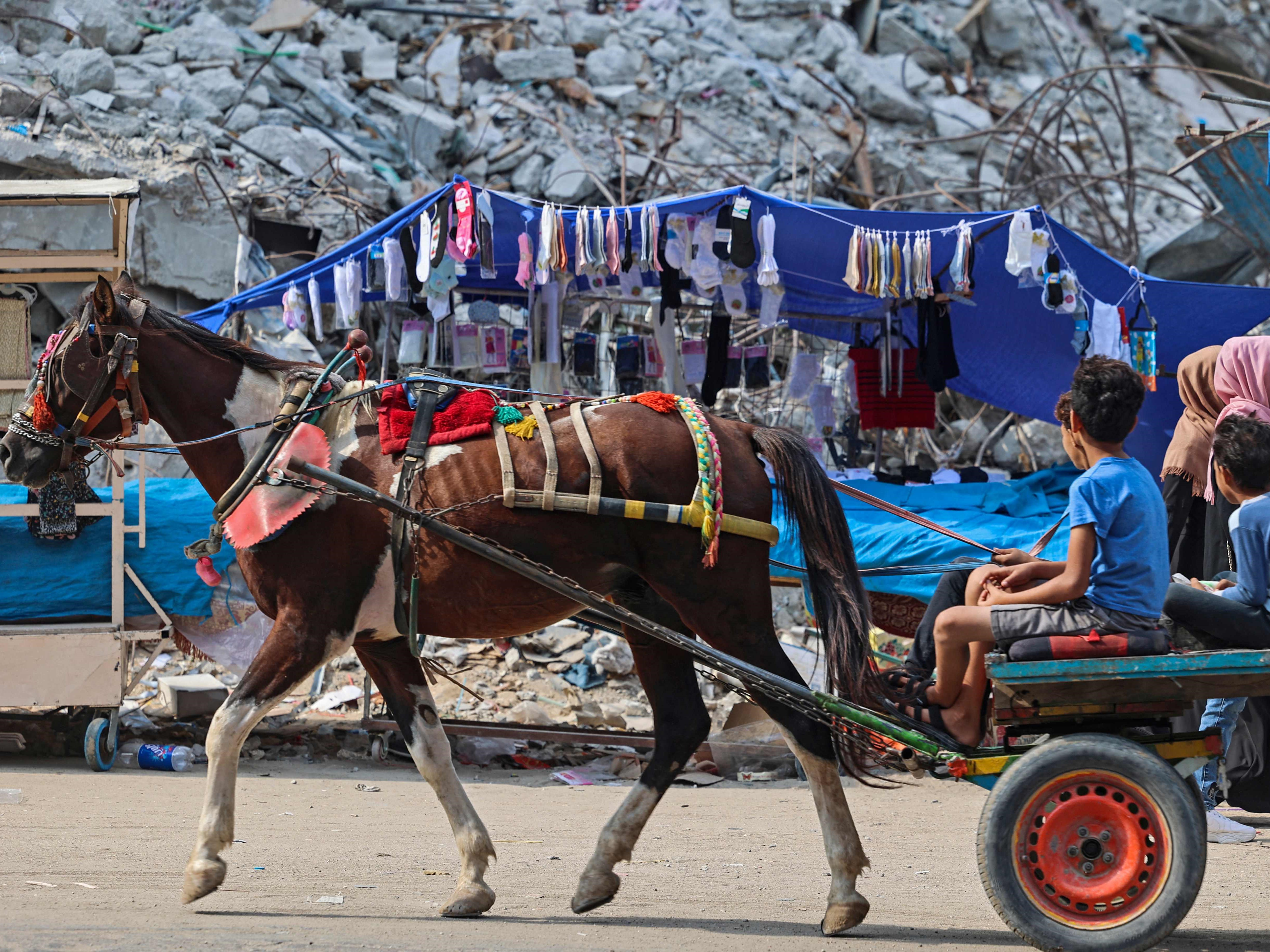 Pemuda Palestina mengendarai kereta kuda melewati bangunan yang hancur di Kota Gaza pada Selasa (5/10). 