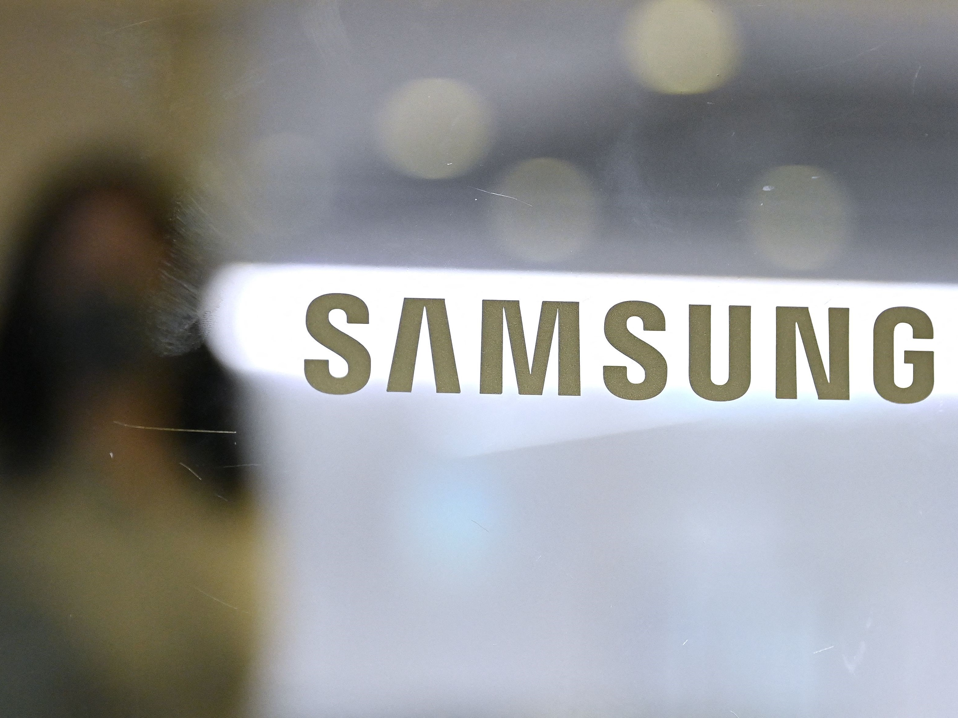 Seorang wanita berjalan melewati logo Samsung yang dipajang di pintu kaca di gedung perusahaan Seocho di Seoul pada Jumat (8/10). 