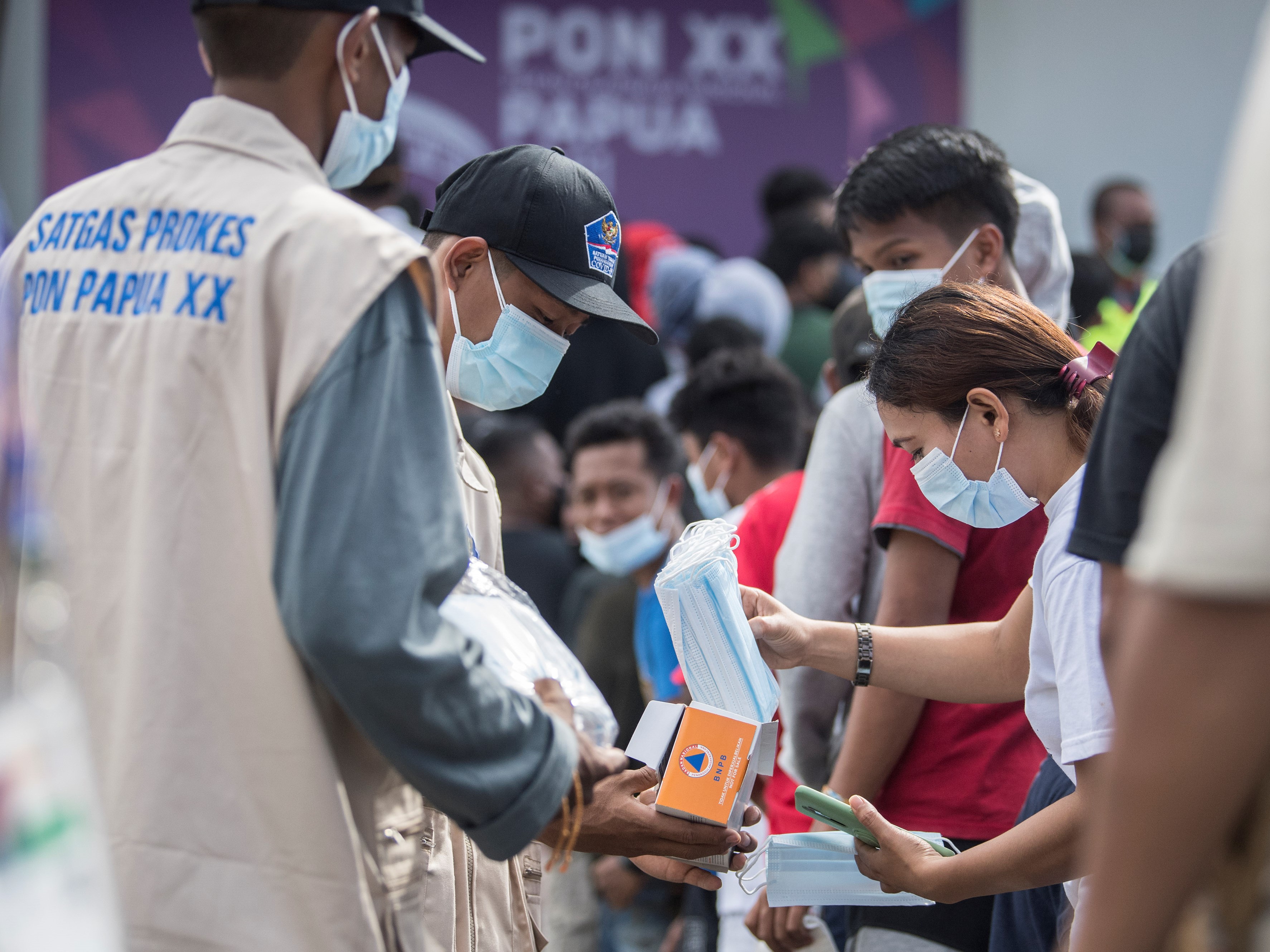 Satgas Prokes membagikan masker kepada warga yang mengantre untuk masuk menyaksikan pertandingan cabang olahraga futsal PON XX Papua.