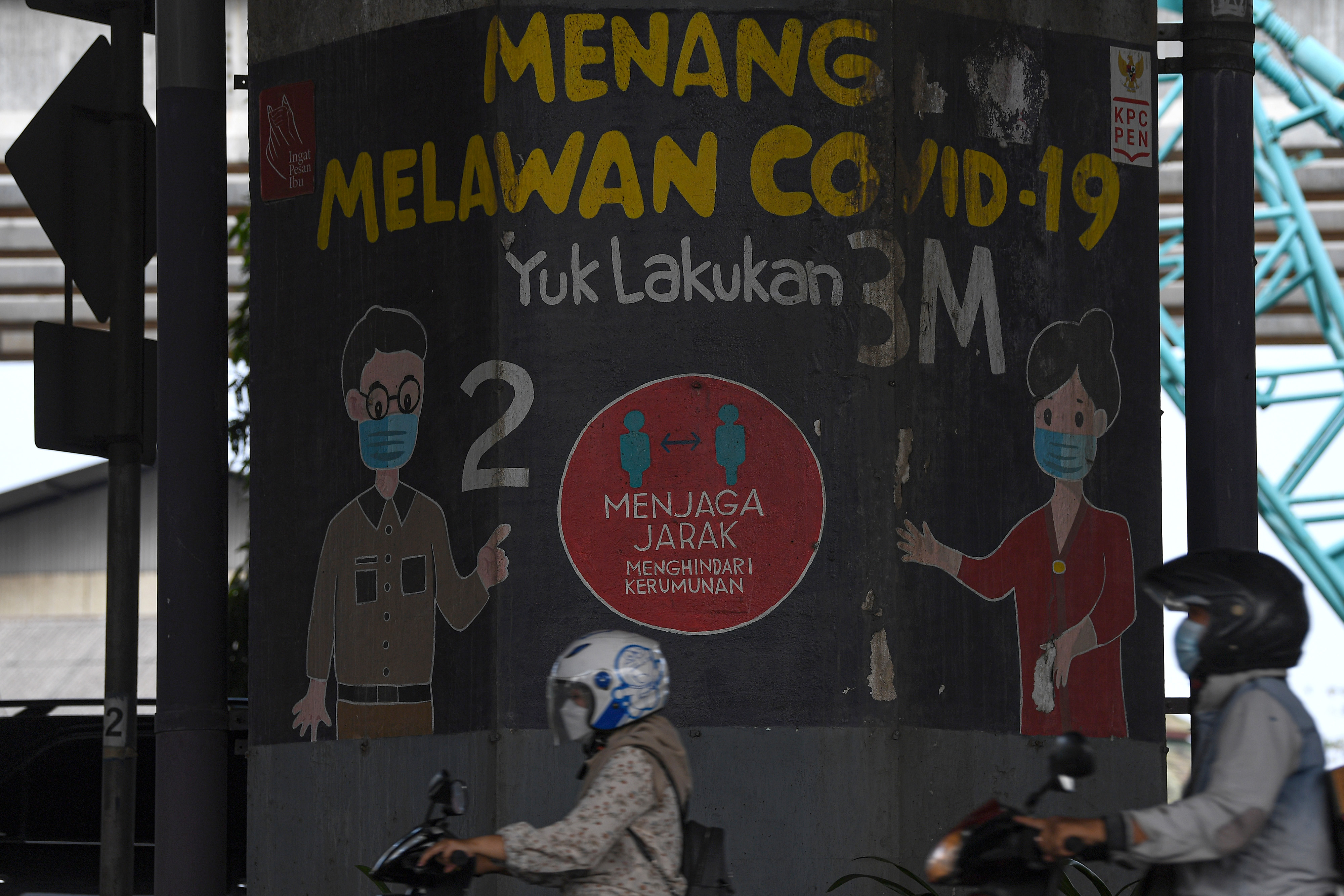Pengendara motor melintasi mural terkait pandemi covid-19 di Jakarta.