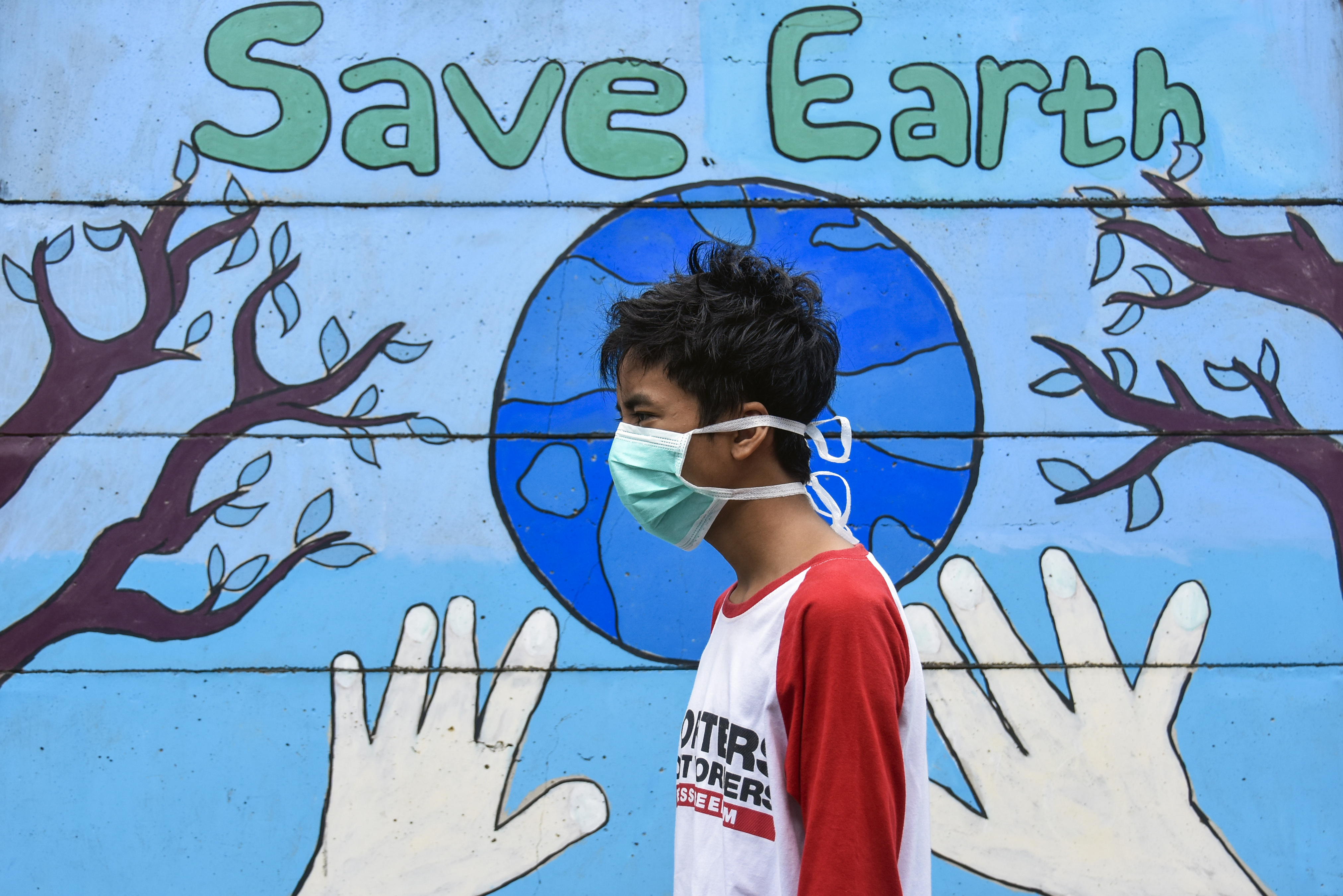 Seorang laki-laki melintas dekat mural bertuliskan Save Earth di Lingkungan Peresak Tempit, Mataram, NTB, Minggu (5/4/20).
