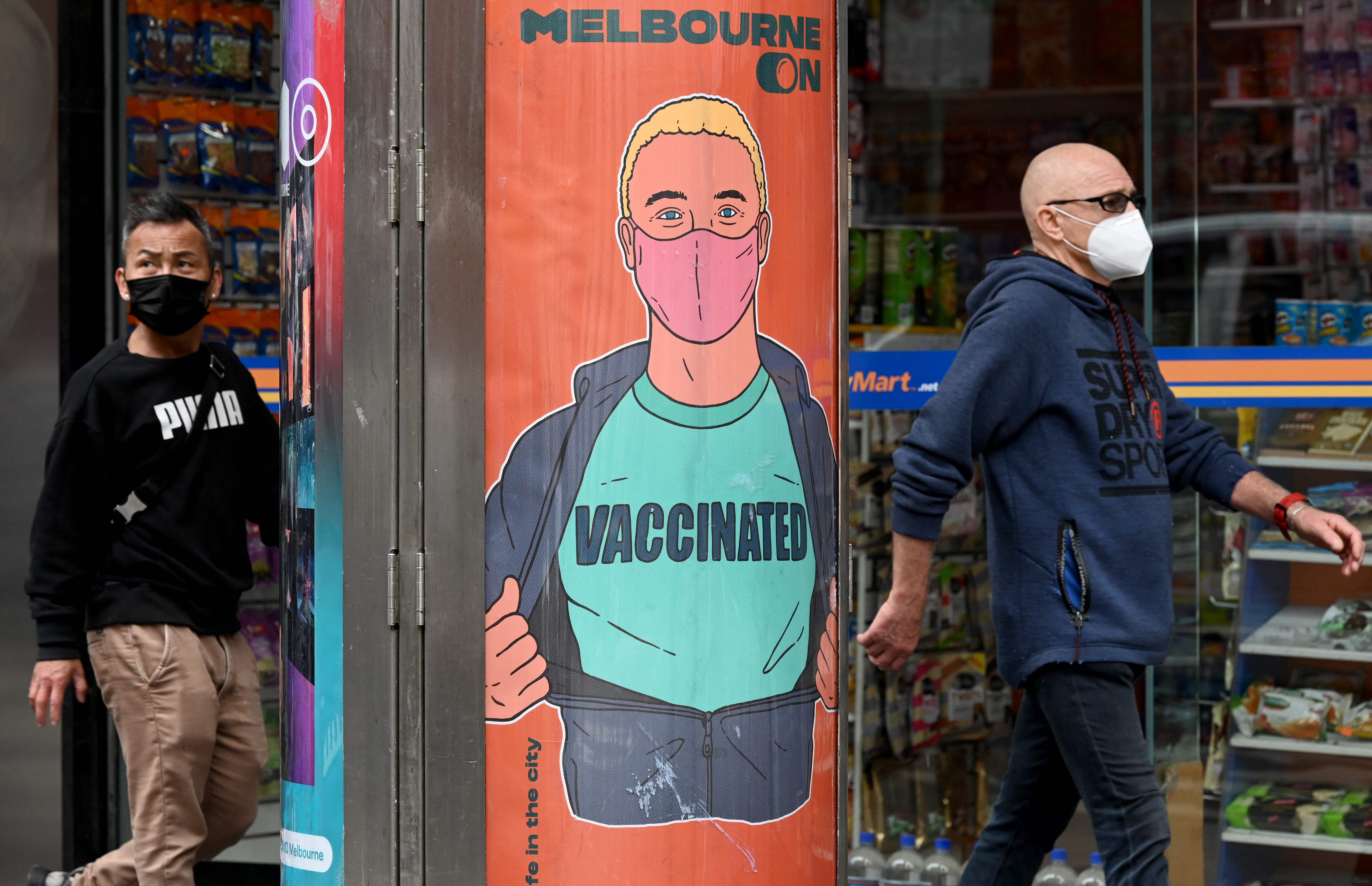 Warga berjalan melintas di depan poster imbauan vaksinasi di Melbourne, Australia.