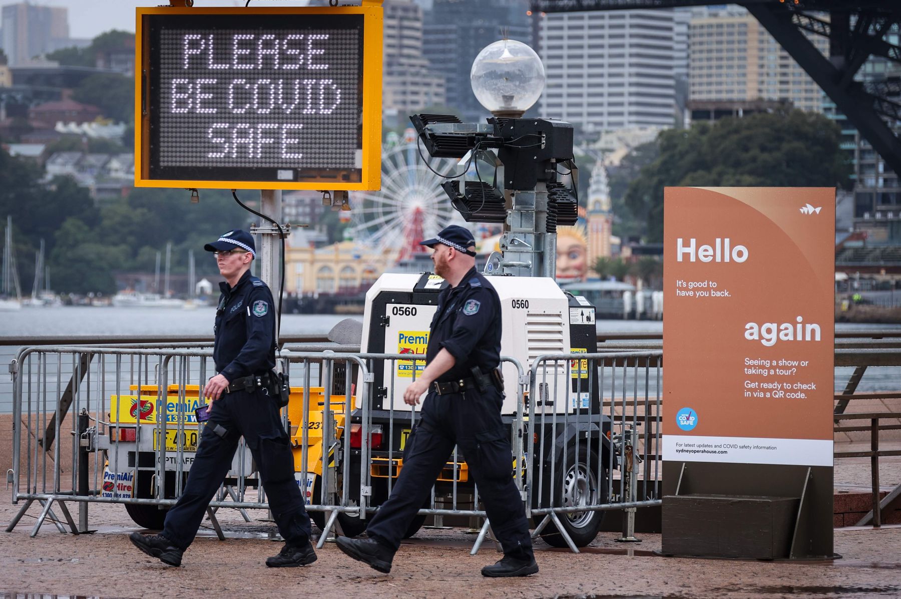 Dua polisi New South Wales melewati gedung dengan papan pengumuman meminta cegah Covid-19 di Sydney, New South Wales, Australia.  