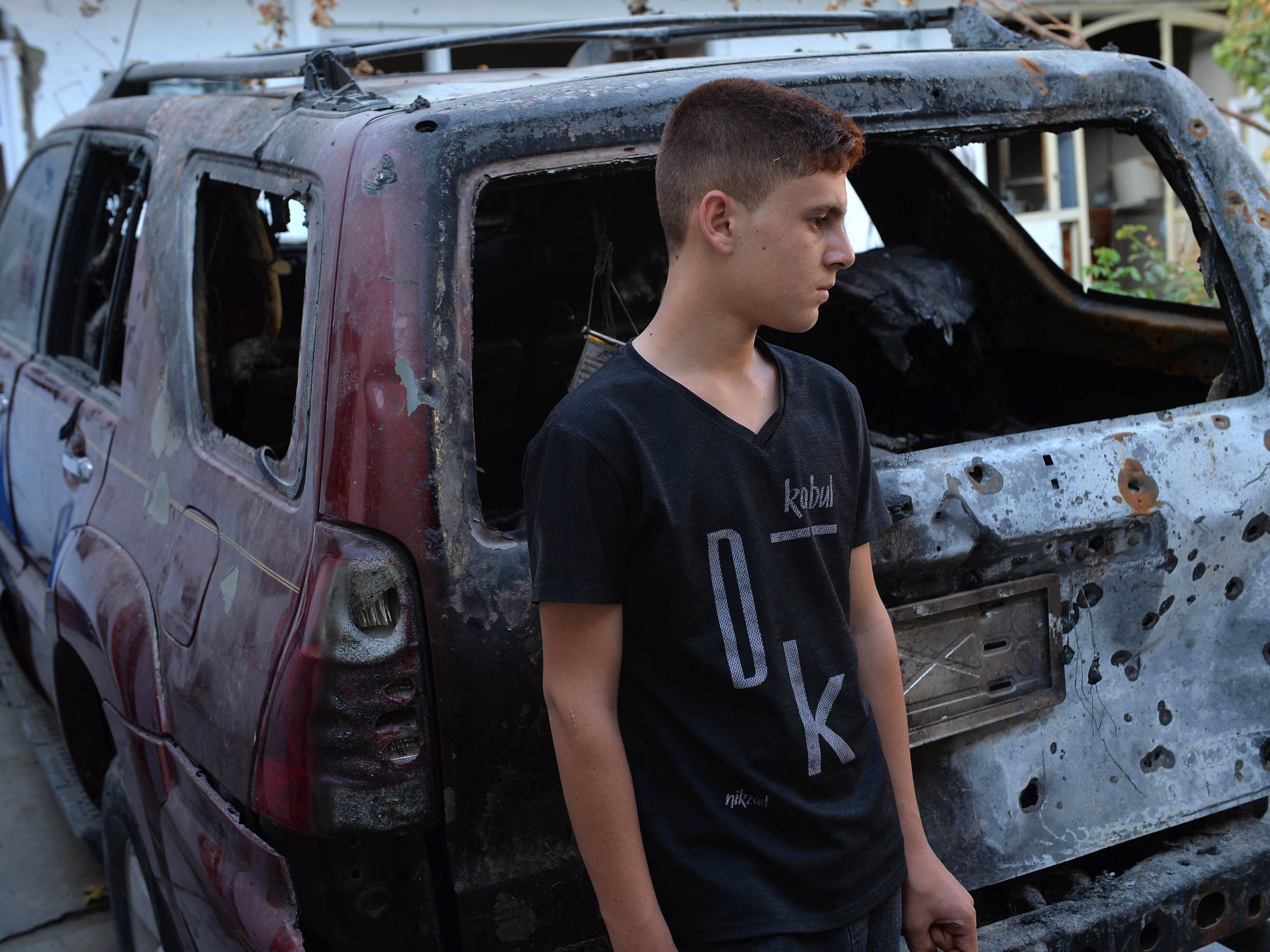 Seorang kerabat Ezmarai Ahmadi berdiri di samping kendaraan yang hancur dalam serangan pesawat tak berawak AS di lingkungan Kwaja Burga.