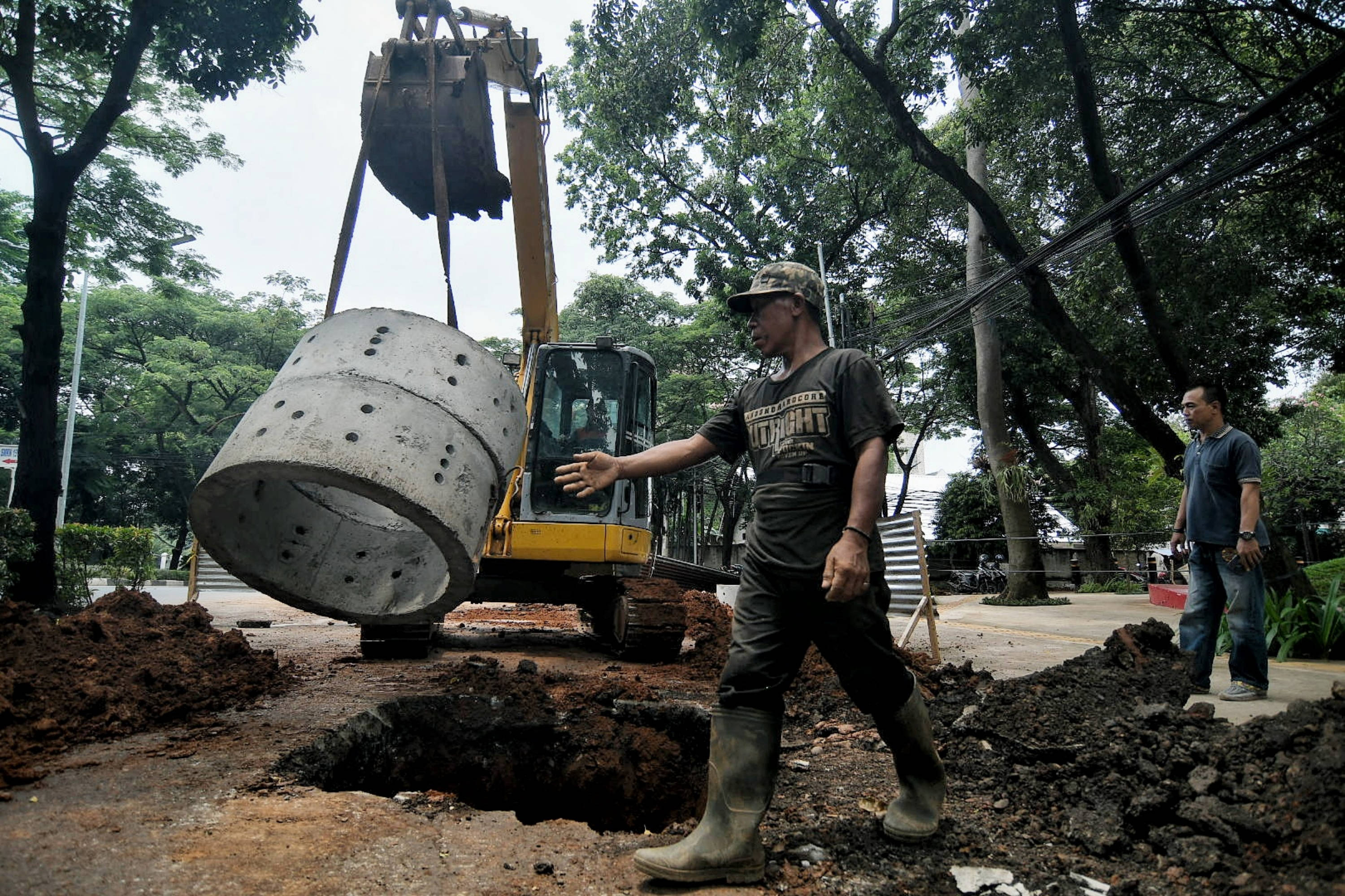 IlustrPekerja menggunakan alat berat saat menyelesaikan pengerjaan sumur resapan di Jalan Mataram Raya, Kebayoran Baru, Jakarta.asi--
