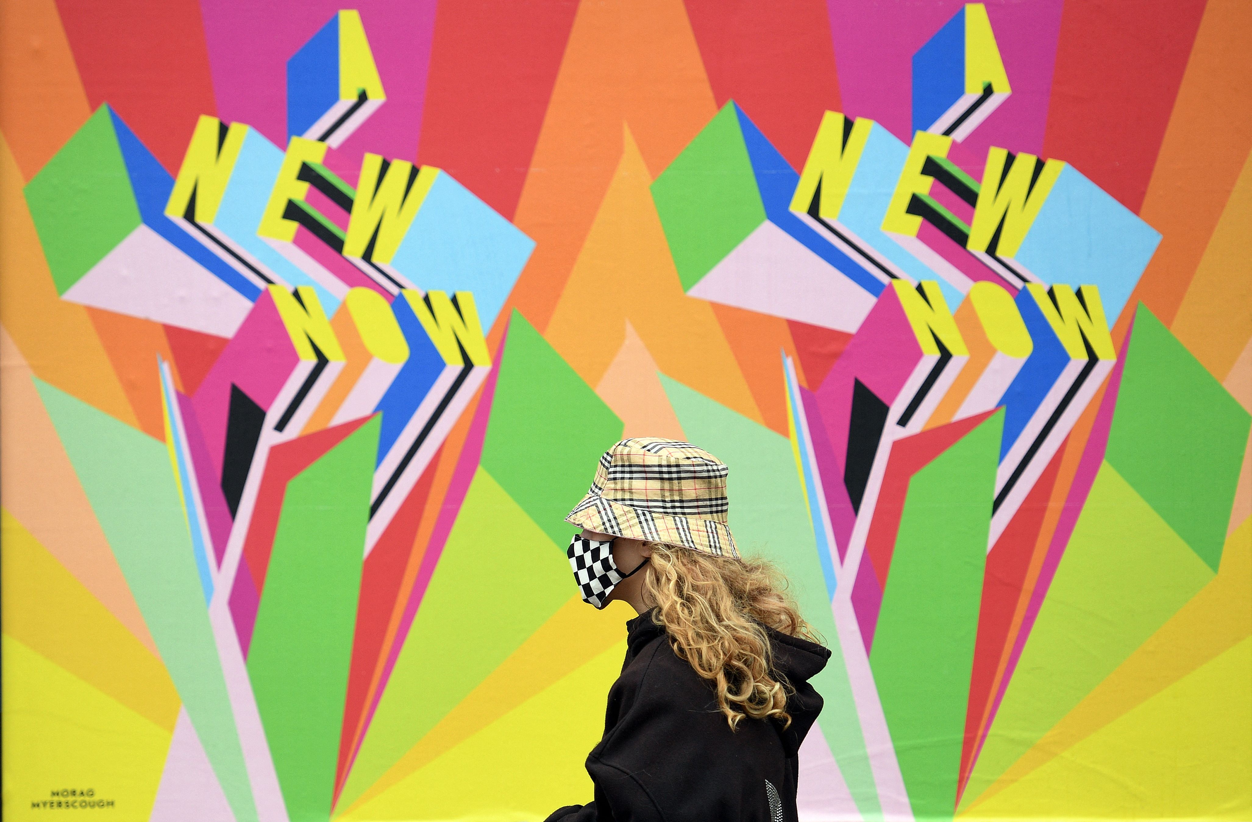 Seorang warga melintas di baliho mengingatkan kebiasan baru saat pandemi covid-19, d inorthern Inggris.