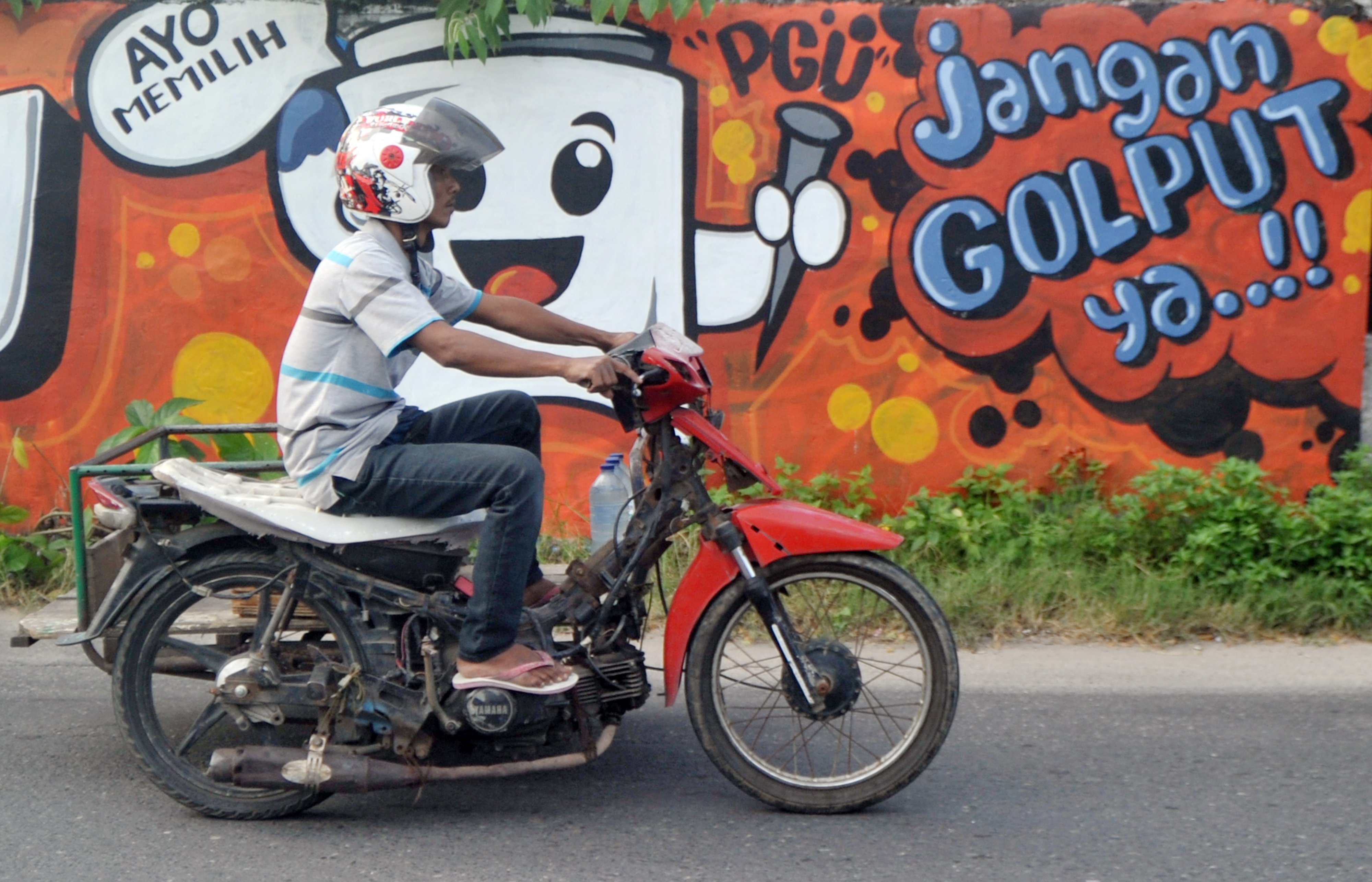 Pengendara melintasi mural terkait pemilu di Padang, Sumatra Barat.