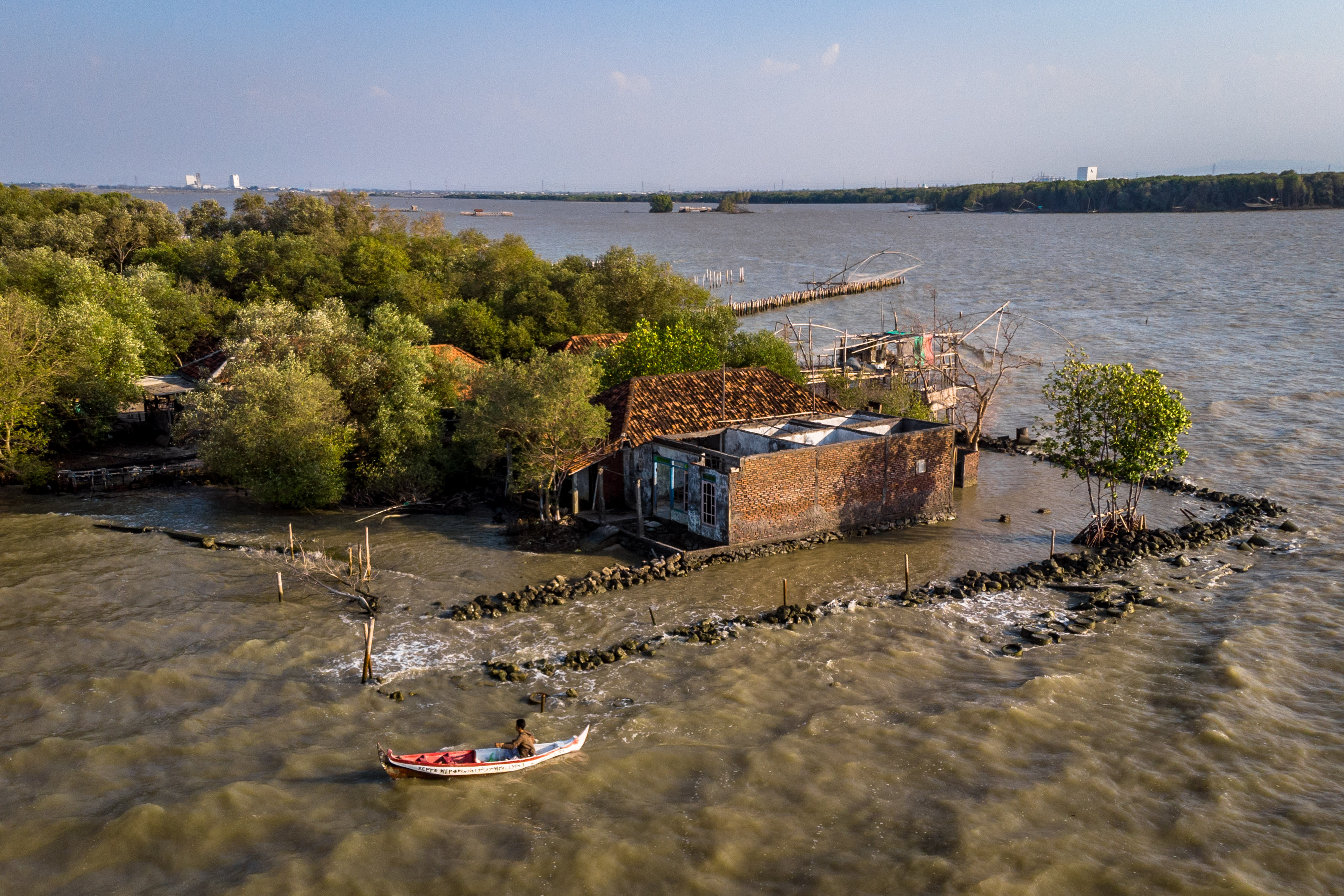  Perahu nelayan melintas di sekitar rumah yang rusak dan ditinggalkan penghuninya akibat abrasi di pesisir Sayung, Demak