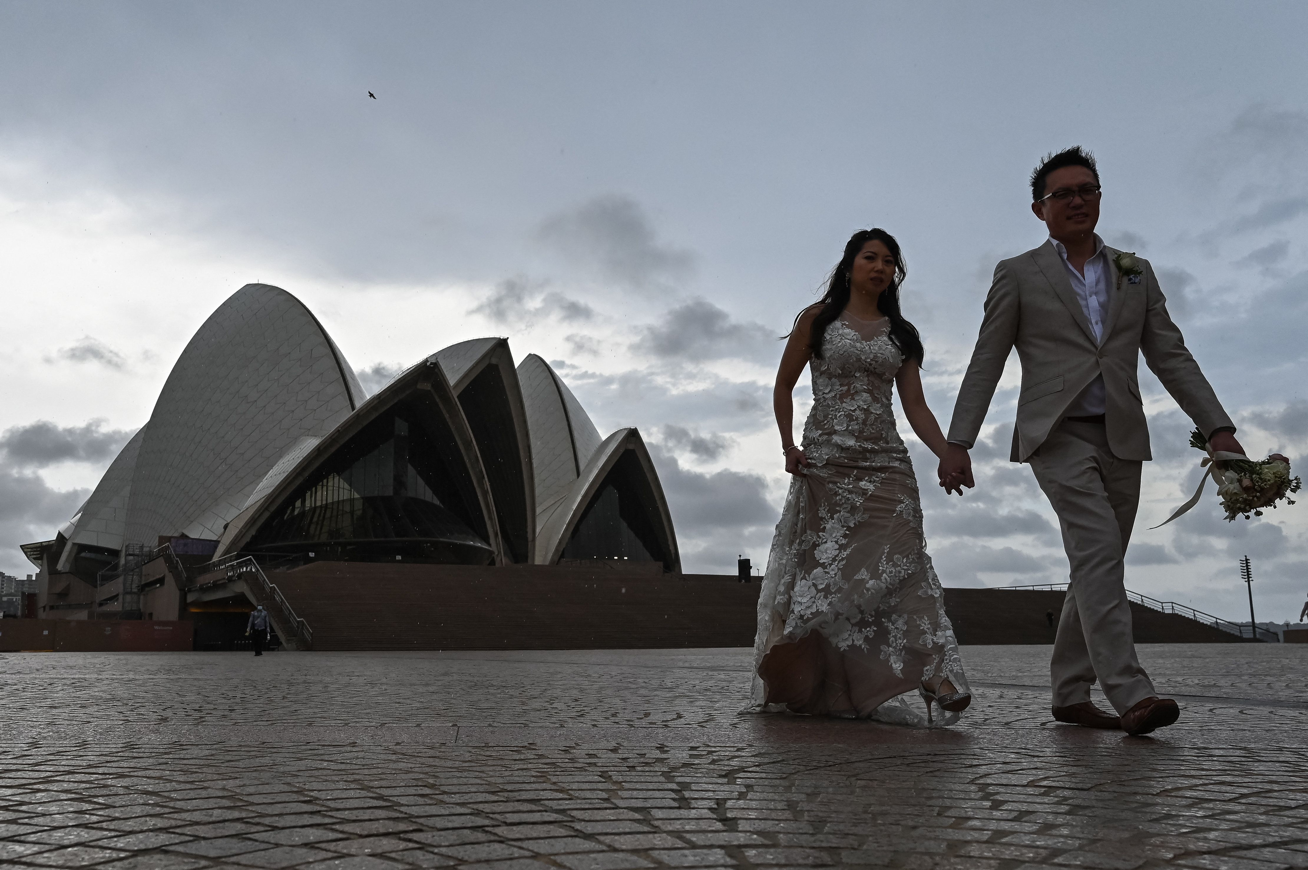 Sepasang pengantin berpose di depan Sydney Opera House, Minggu (10/10), sehari sebelum pencabutan lockdown di kota Australia itu.