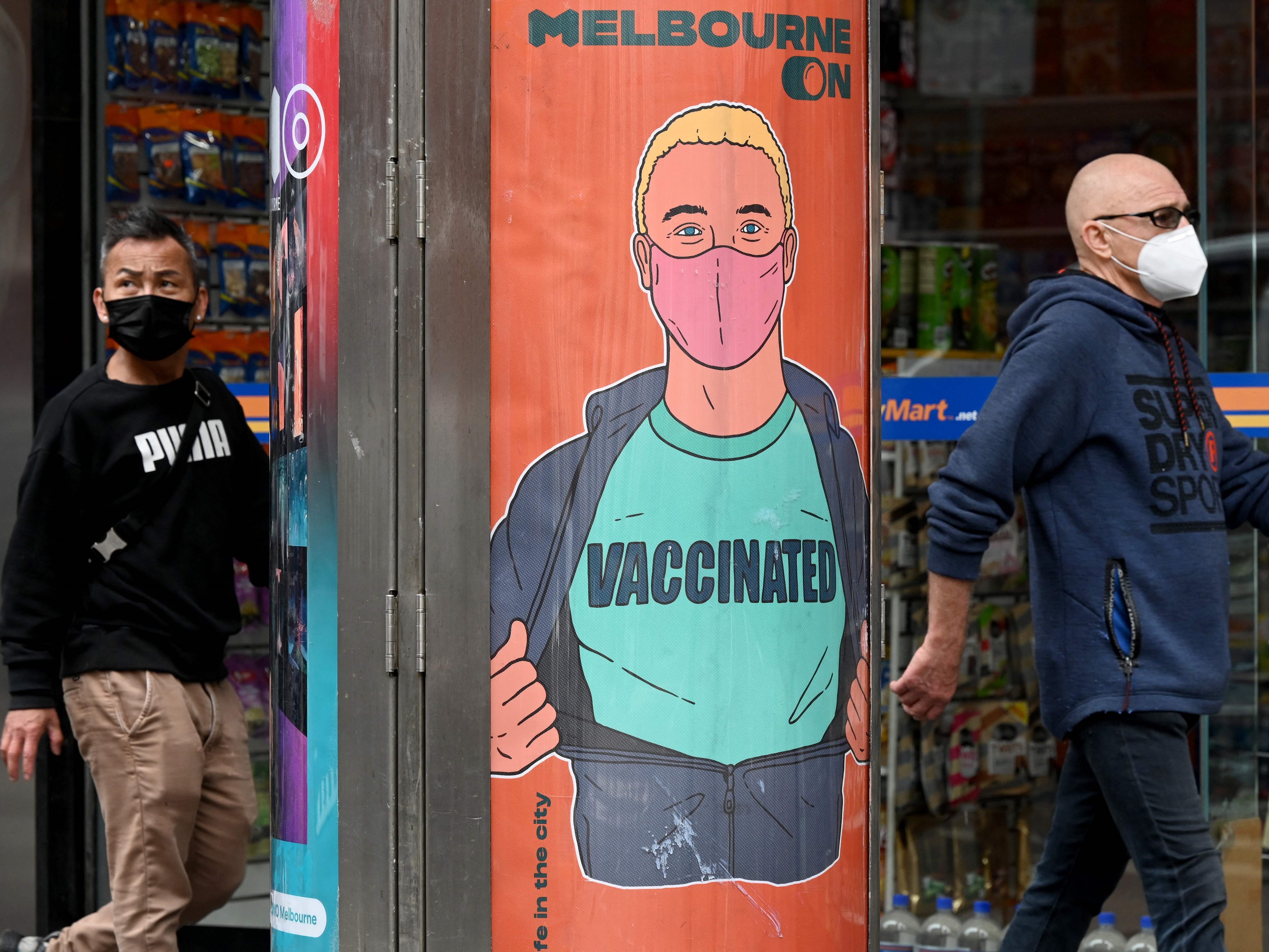 Warga Australia berjalan melalui poster yang mendorong vaksinasi di Melbourne, Kamis (30/9).