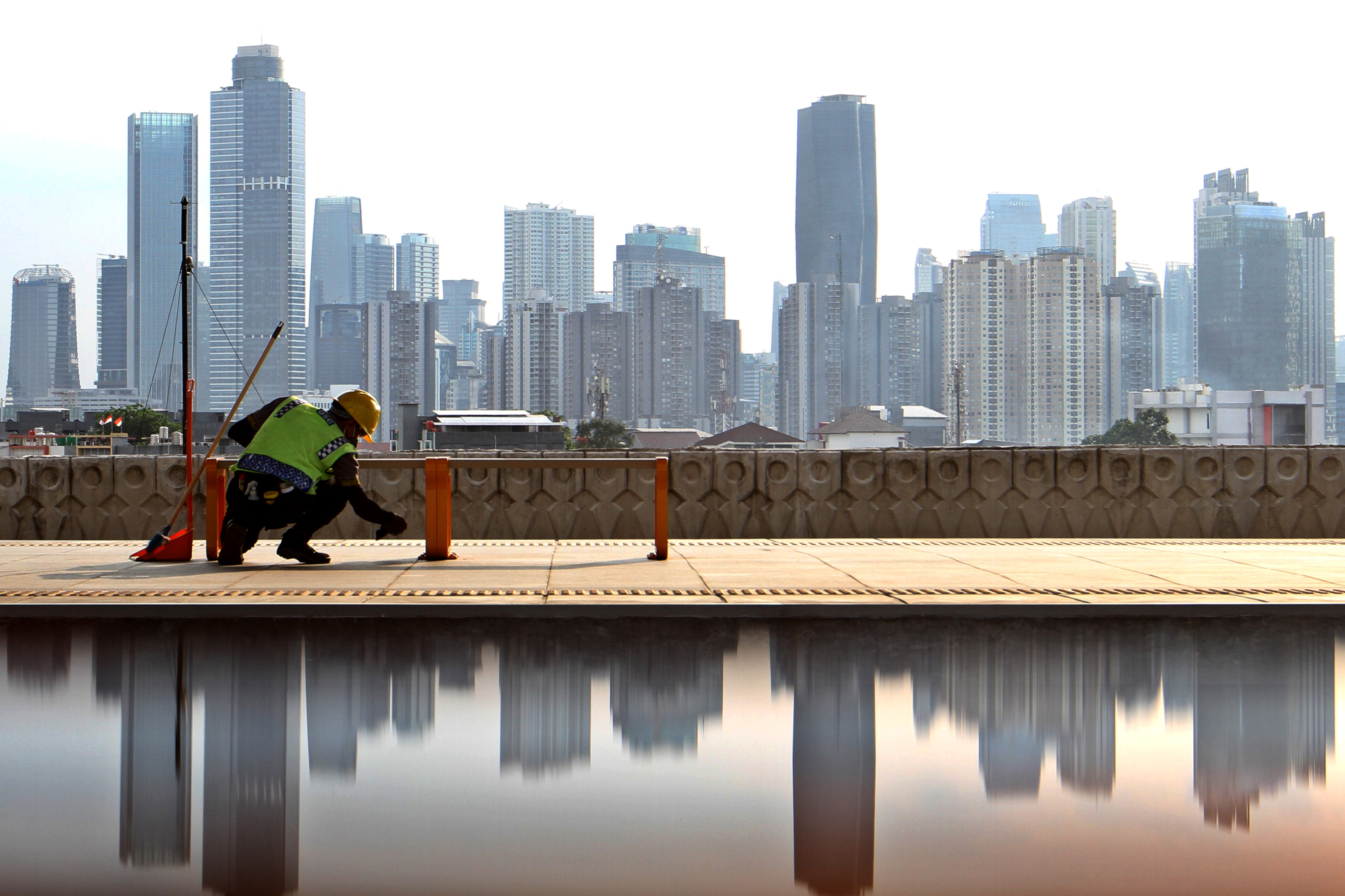 Pekerja membersihkan peron Stasiun Manggarai dengan latar gedung bertingkat di wilayah Jakarta.