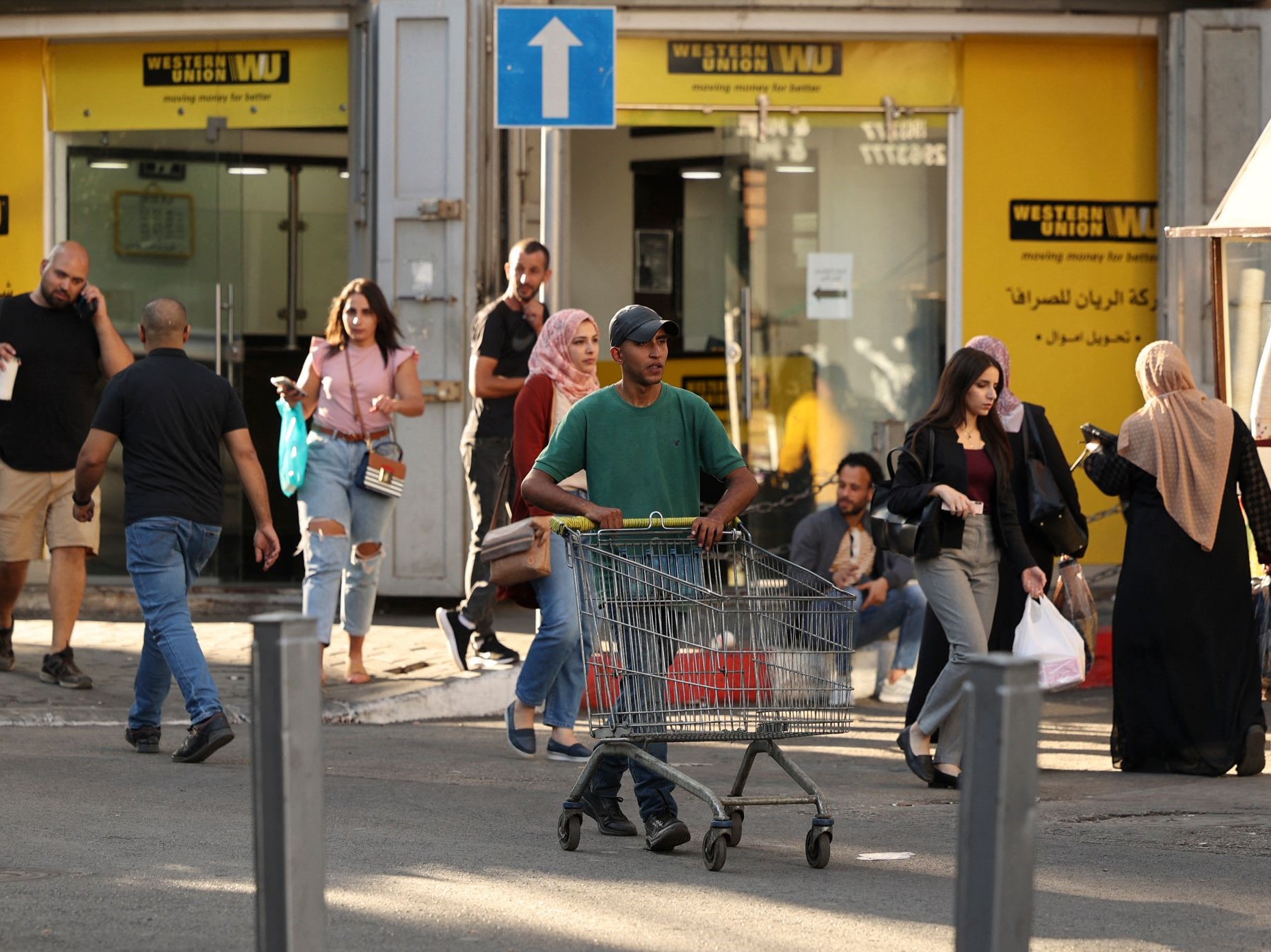 Warga Palestina berjalan di depan loket penukaran mata uang di kota Ramallah Tepi Barat pada 5 Oktober 2021.