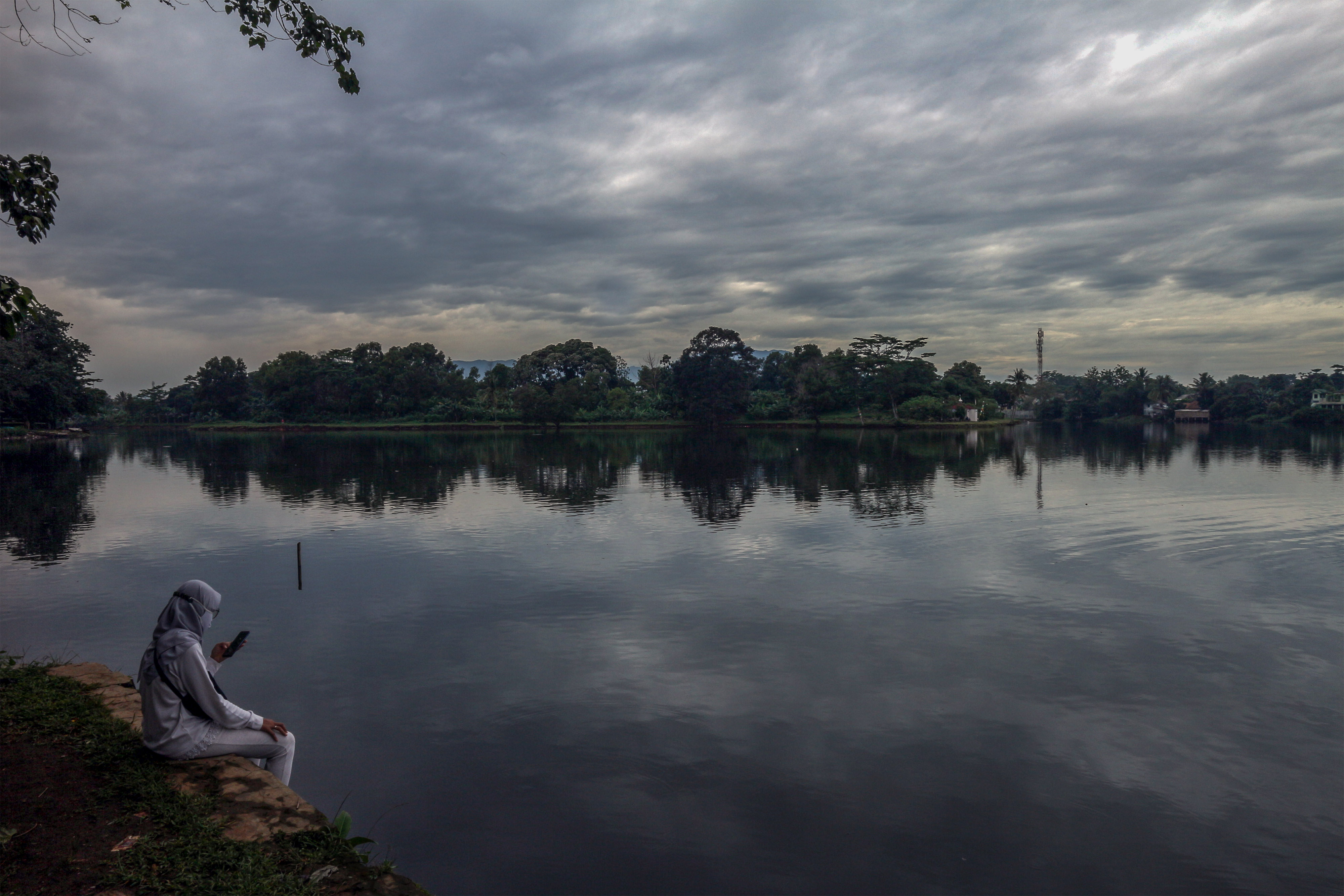 Seorang warga duduk di tepi Situ Cikaret dengan latar belakang awan mendung di Cibinong, Kabupaten Bogor, Jawa Barat, Kamis (11/11/2021)
