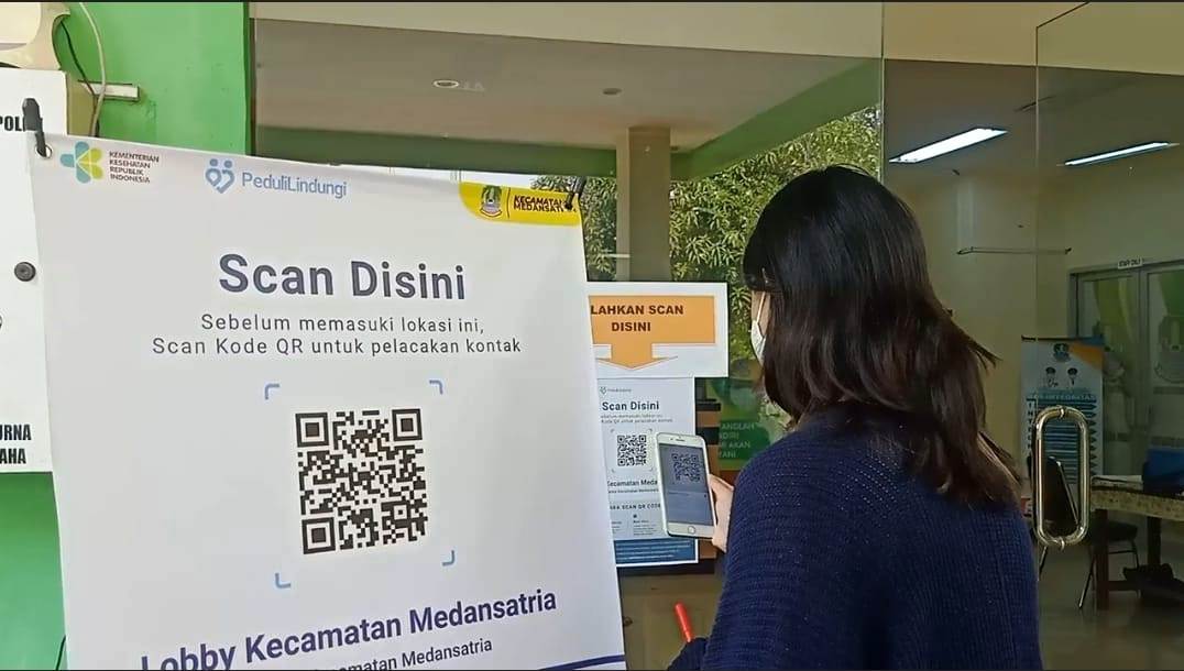 Seorang warga sedang meng-scan barcode PeduliLindungi.
