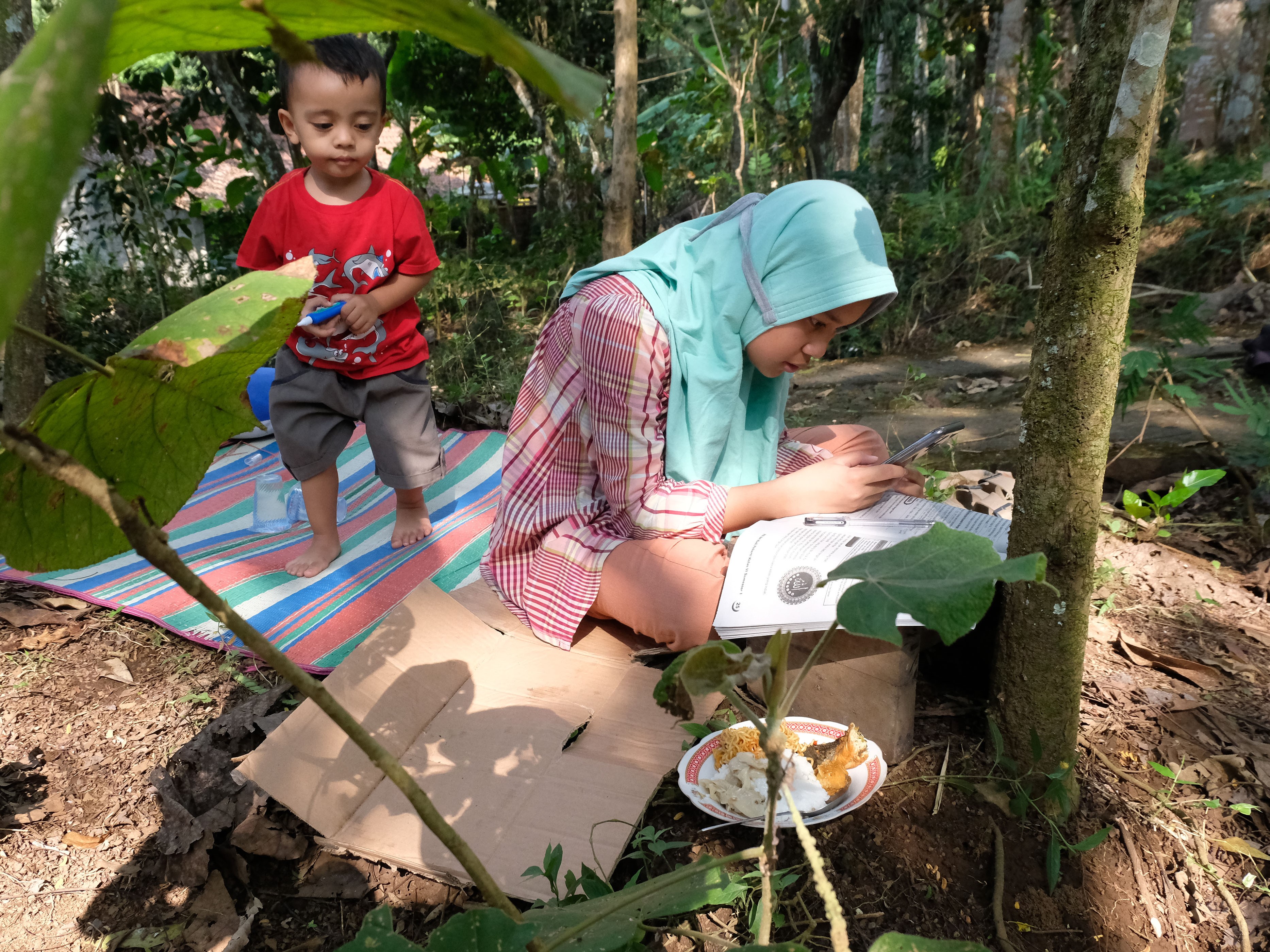 Pelajar kelas 6 SD Nadhifa Muazara terpaksa mengerjakan tugas sekolah secara daring di perkebunan karena kesulitan sinyal internet.