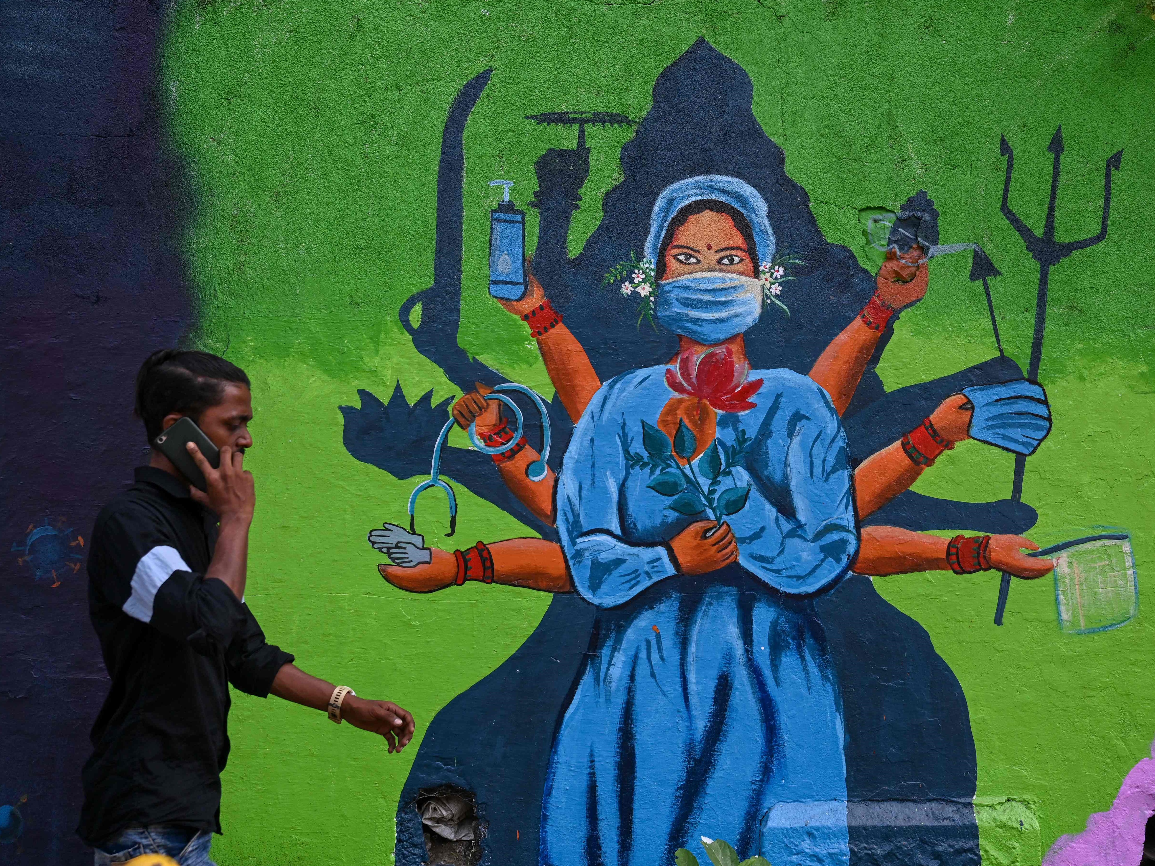 Seorang pria berjalan melewati mural dinding yang menggambarkan seorang petugas kesehatan sebagai Dewi Durga Hindu.