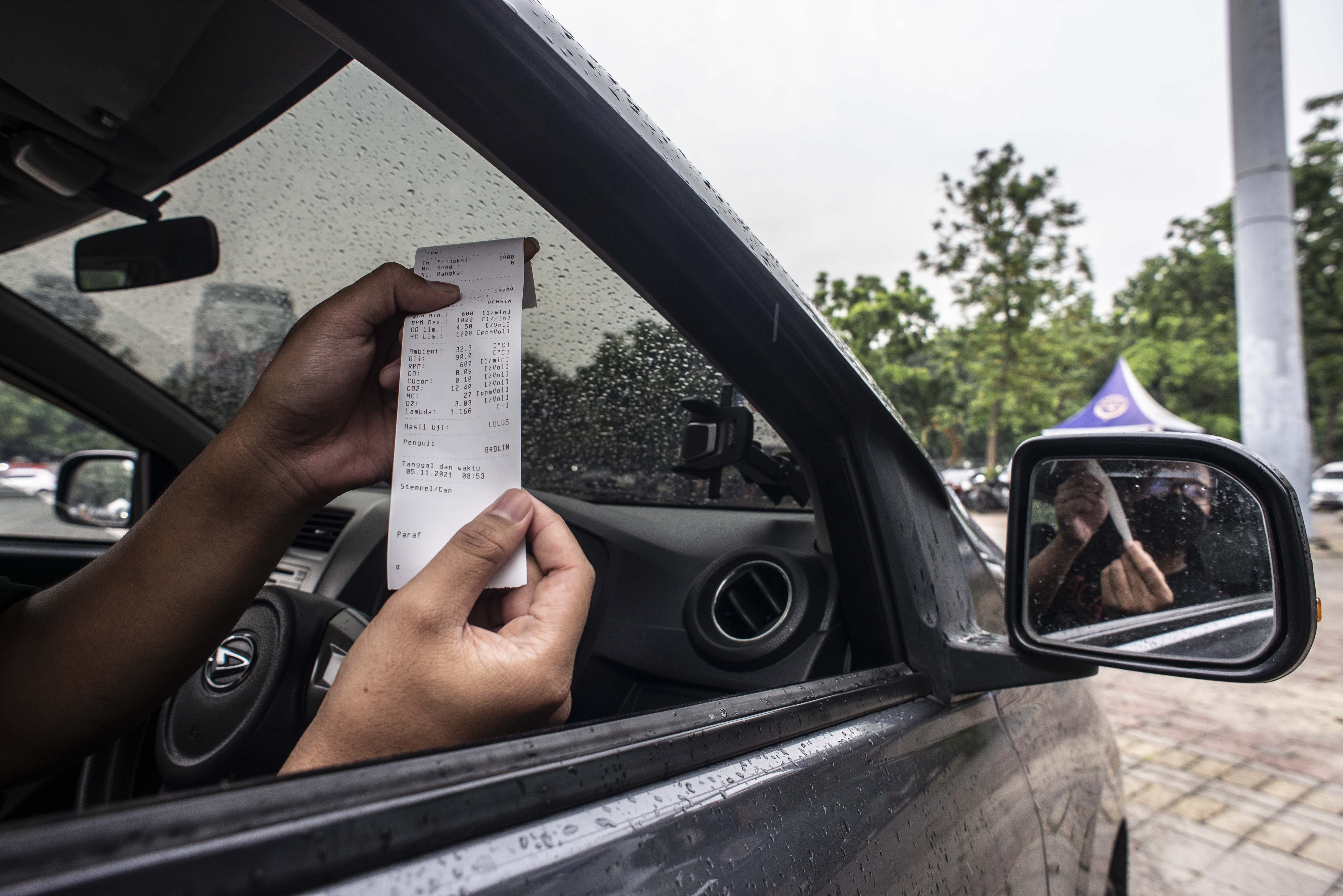 Pengemudi menujukkan hasil uji emisi kendaraan bermotor miliknya di kawasan IRTI Monas, Jakarta