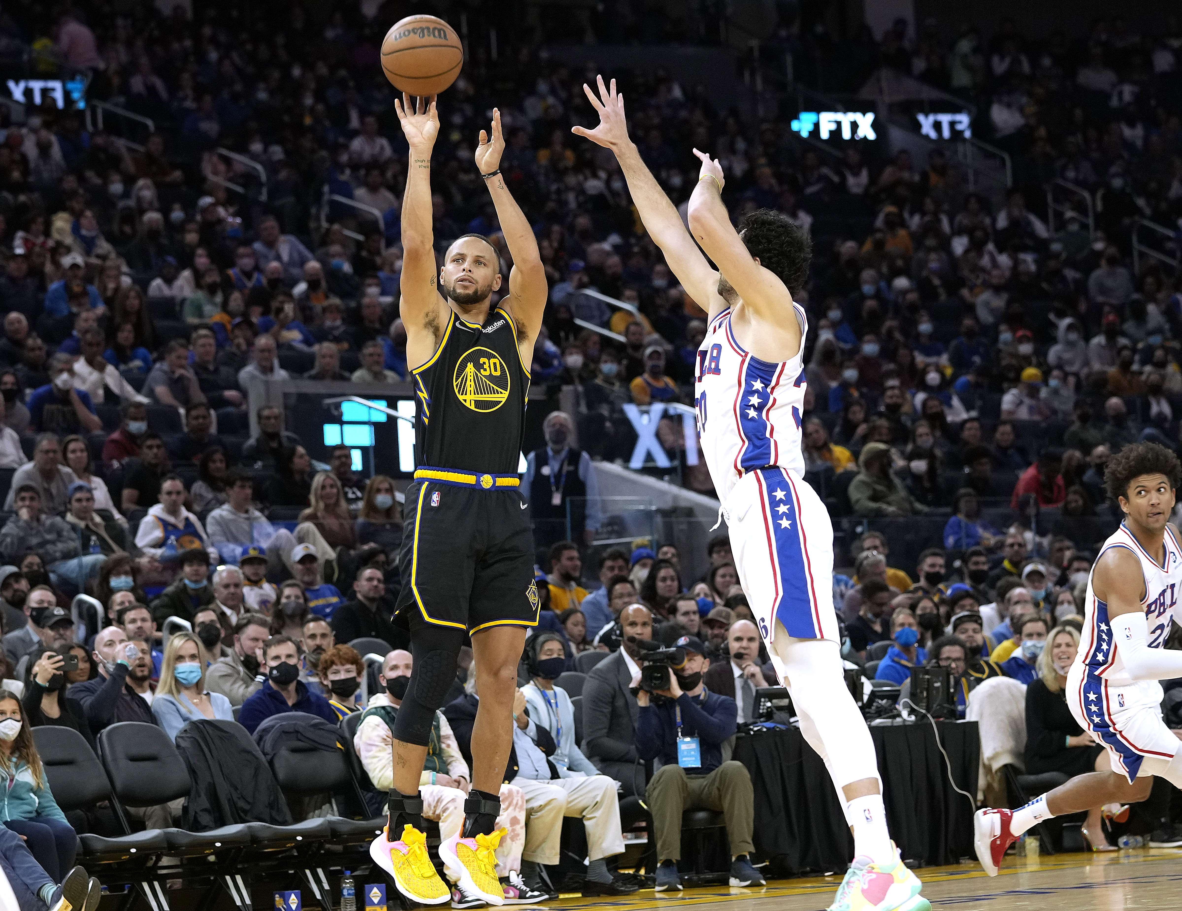 Stephen Curry (kiri) dari Golden State Warriors melakukan tembakan dengan dihalangani Furkan Korkmaz dari Philadelphia 76ers.