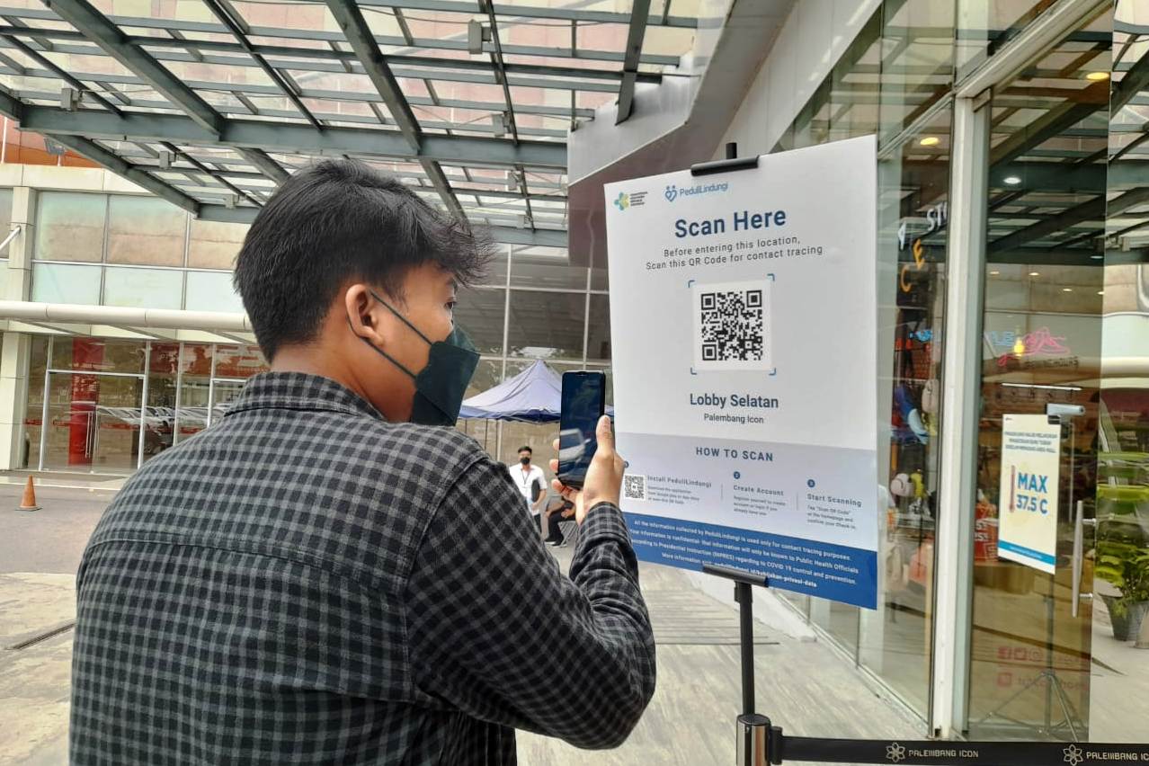 Pengunjung mal Palembang Icon sedang melakukan scan aplikasi PeduliLindungi yang disediakan di pintu masuk mal.