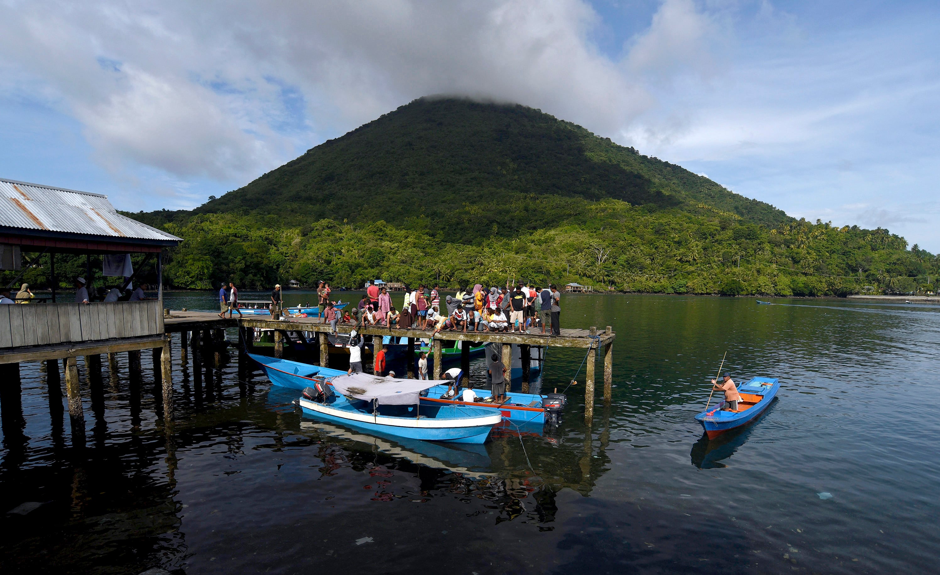 Warga membeli ikan dari nelayan di Dermaga Banda Naira, Maluku dengan latar belakang Gunung Banda. 