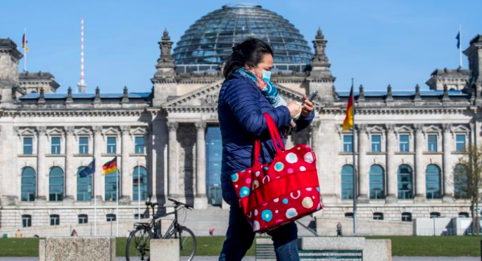 Seorang warga mengenakan masker melintas di depan gedung parlemen Jerman di Berlin.