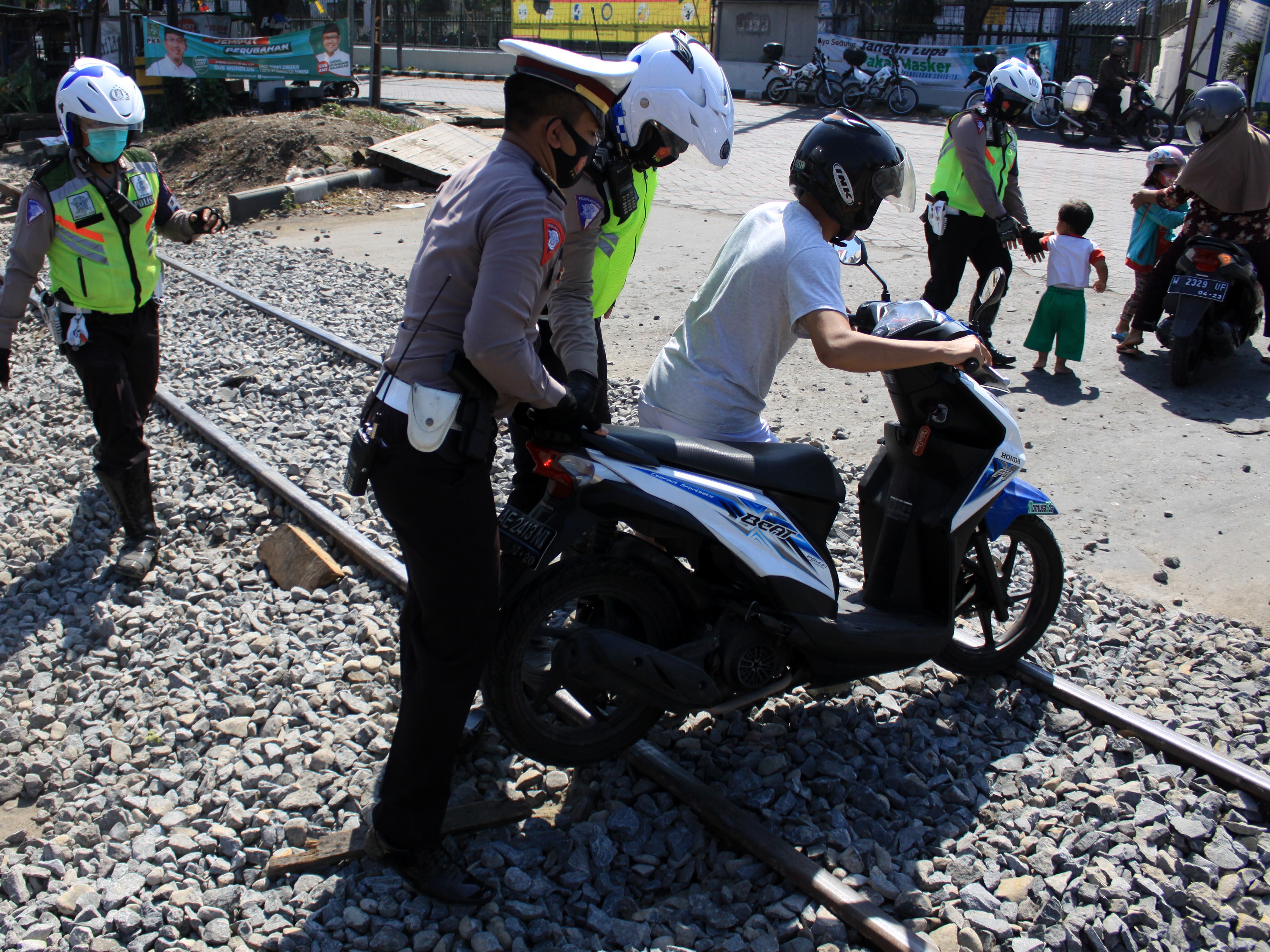 Anggota Satlantas Polresta Sidoarjo membantu pengendara mendorong sepeda motor yang melintas di atas jalur rel yang sedang diperbaiki.