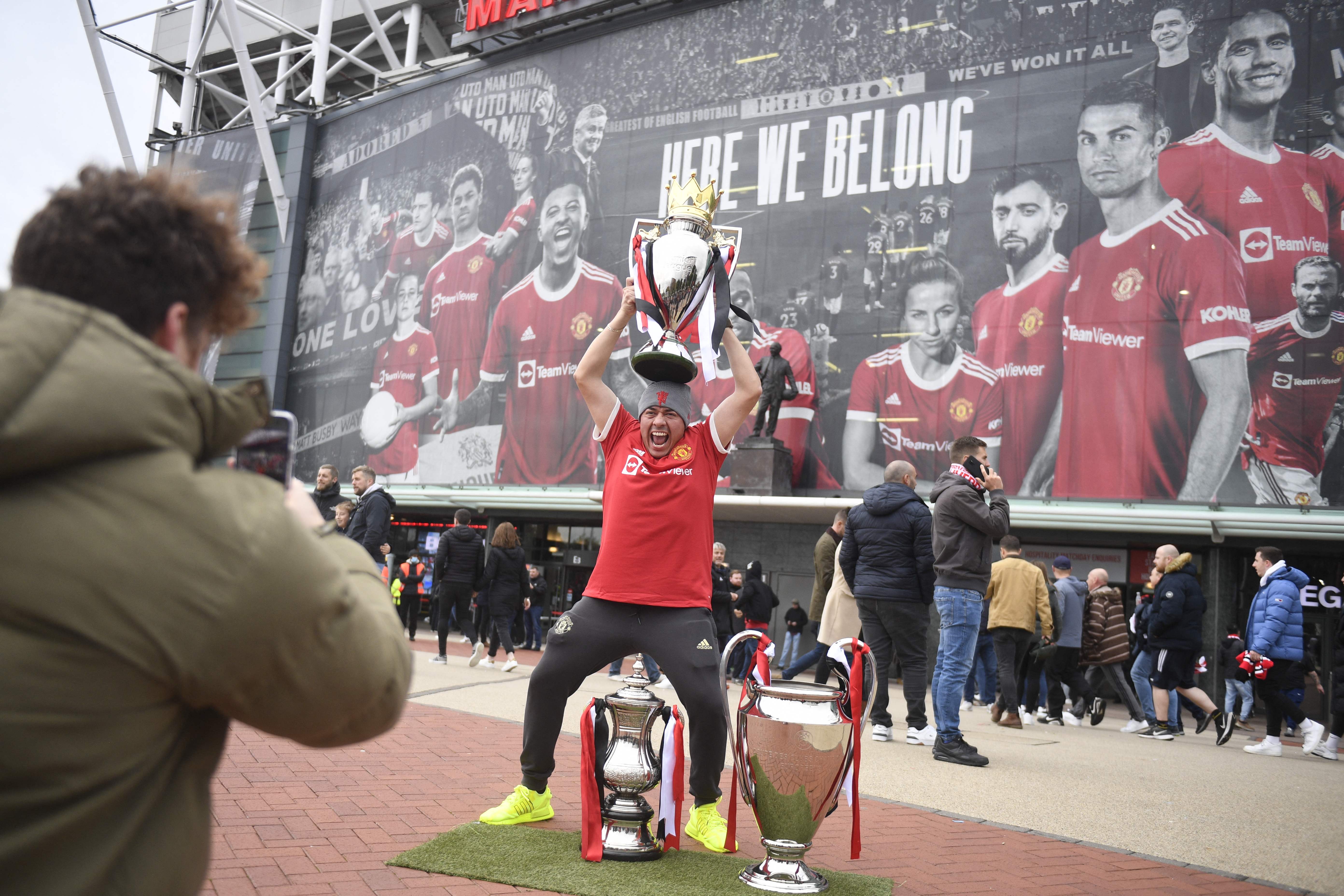 Seorang pendukung Manchester United berpose dengan replika trofi Liga Primer Inggris di depan Old Trafford.