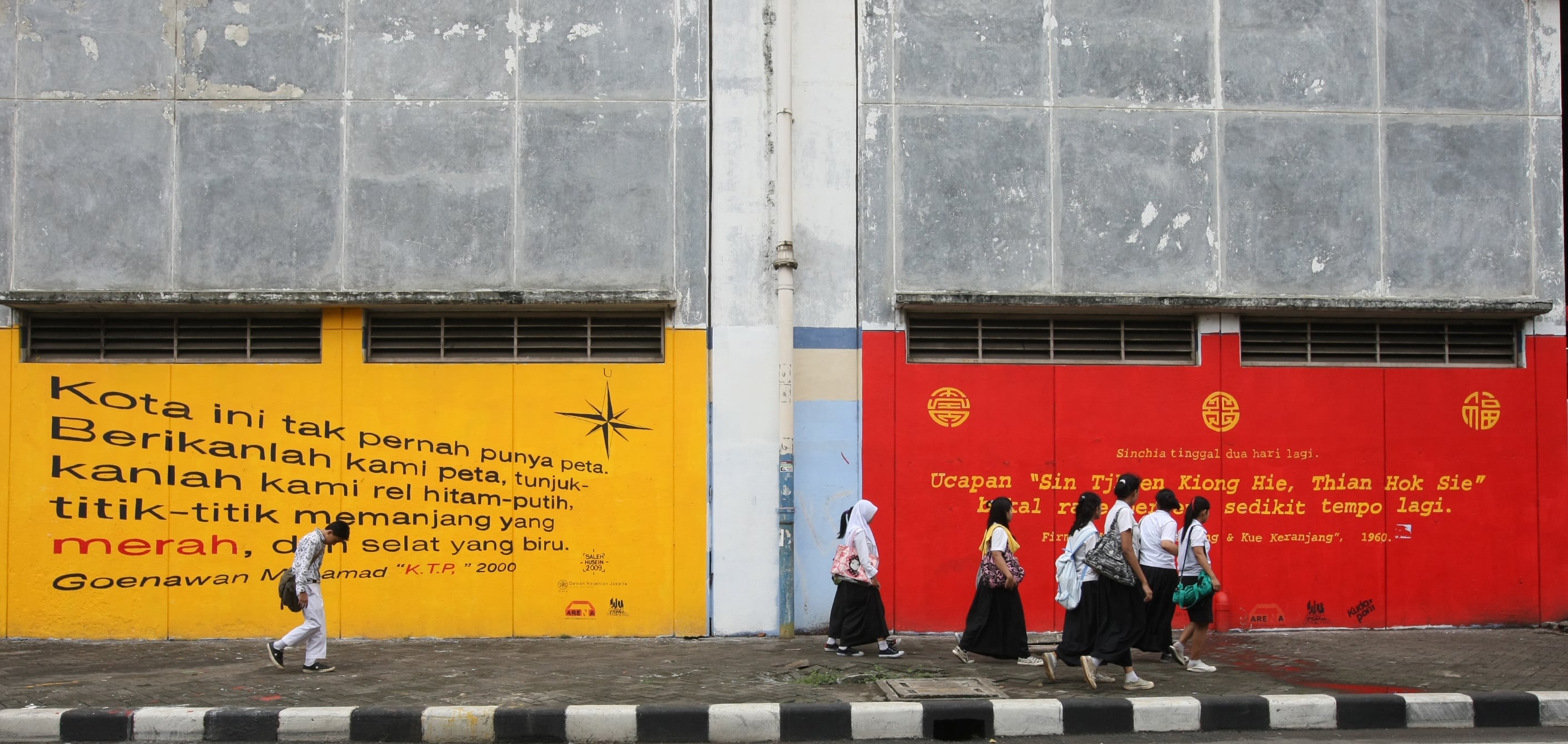 Sejumlah anak sekolah melintas di trotoar dengan latar belakang mural yang bertuliskan bait puisi maupun prosa yang bertemakan Kota Jakarta 