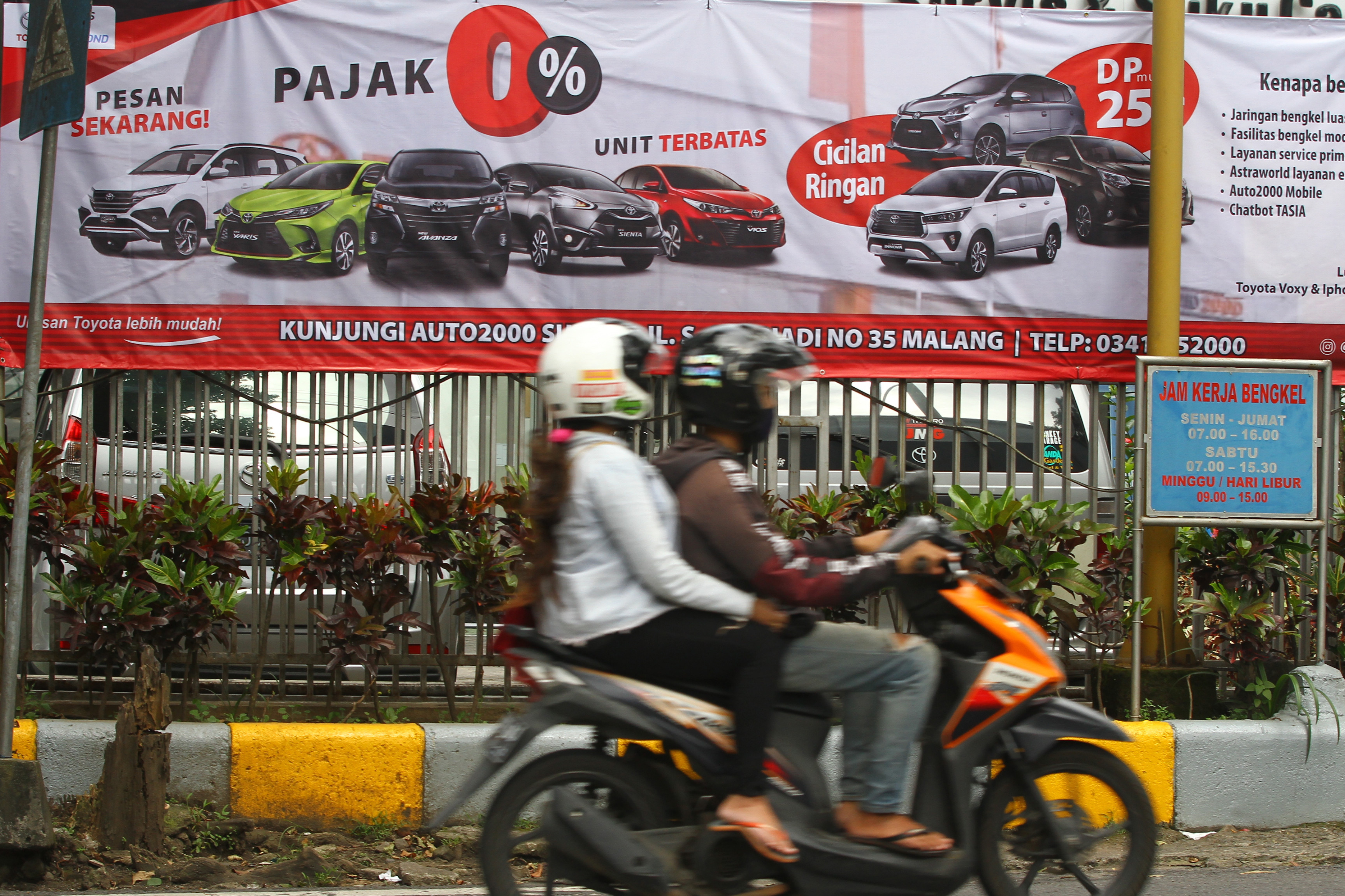 Pengendara motor melintas di depan spanduk insentif pajak untuk pembelian mobil