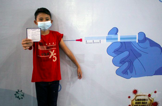 seorang anak menunjukkan kartu vaksinasi covid-19.