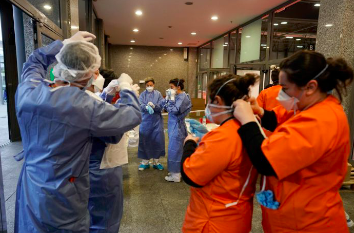 Petugas medis saling membantu mempersiapkan diri sebelum menjalankan tugas di rumah sakit darurat Covid-19 di Madrid, Spanyol. 
