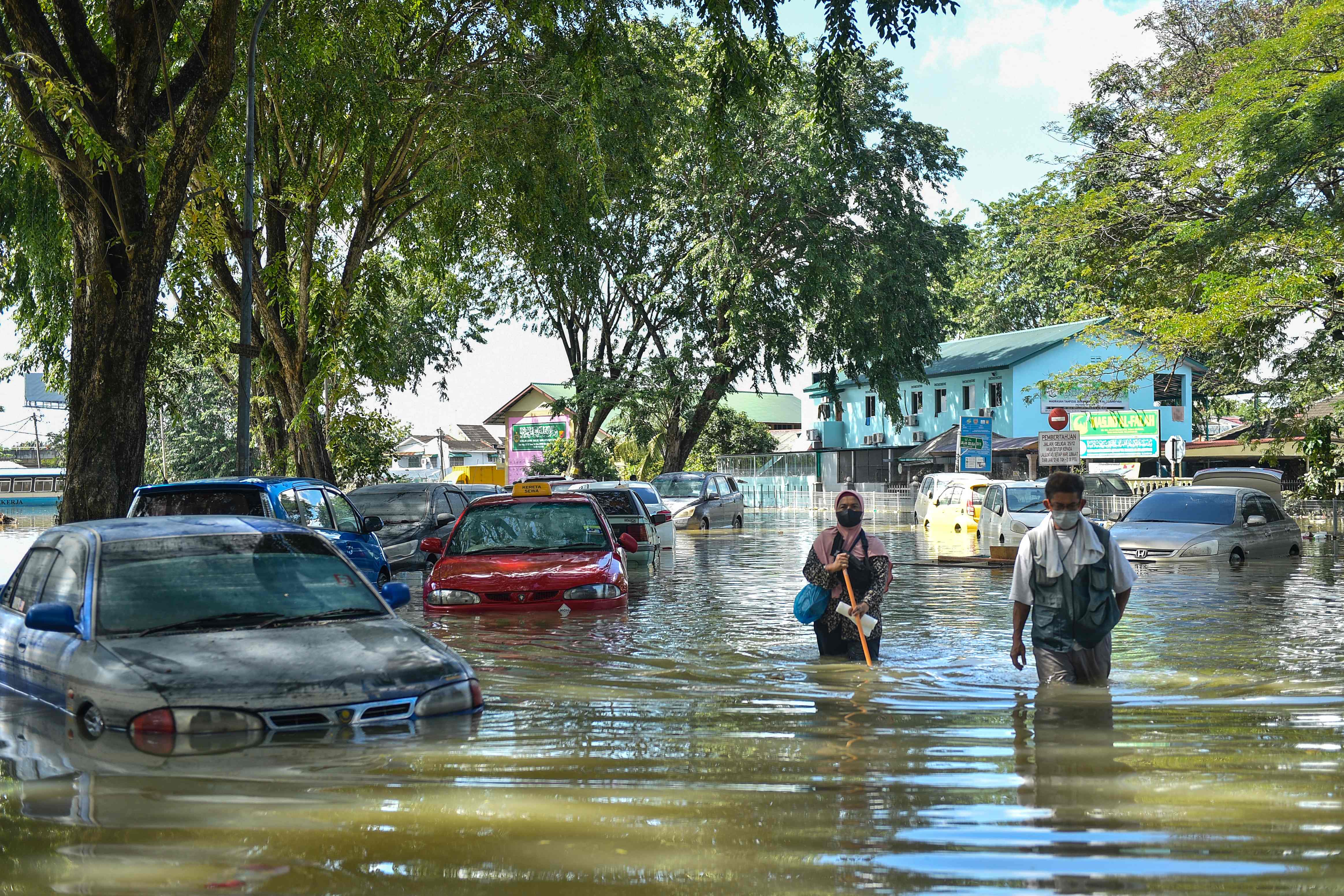 Warga berjalan melintasi mobil-mobil yang terendam banjir di Shah Alam, Selangor, Malaysia.
