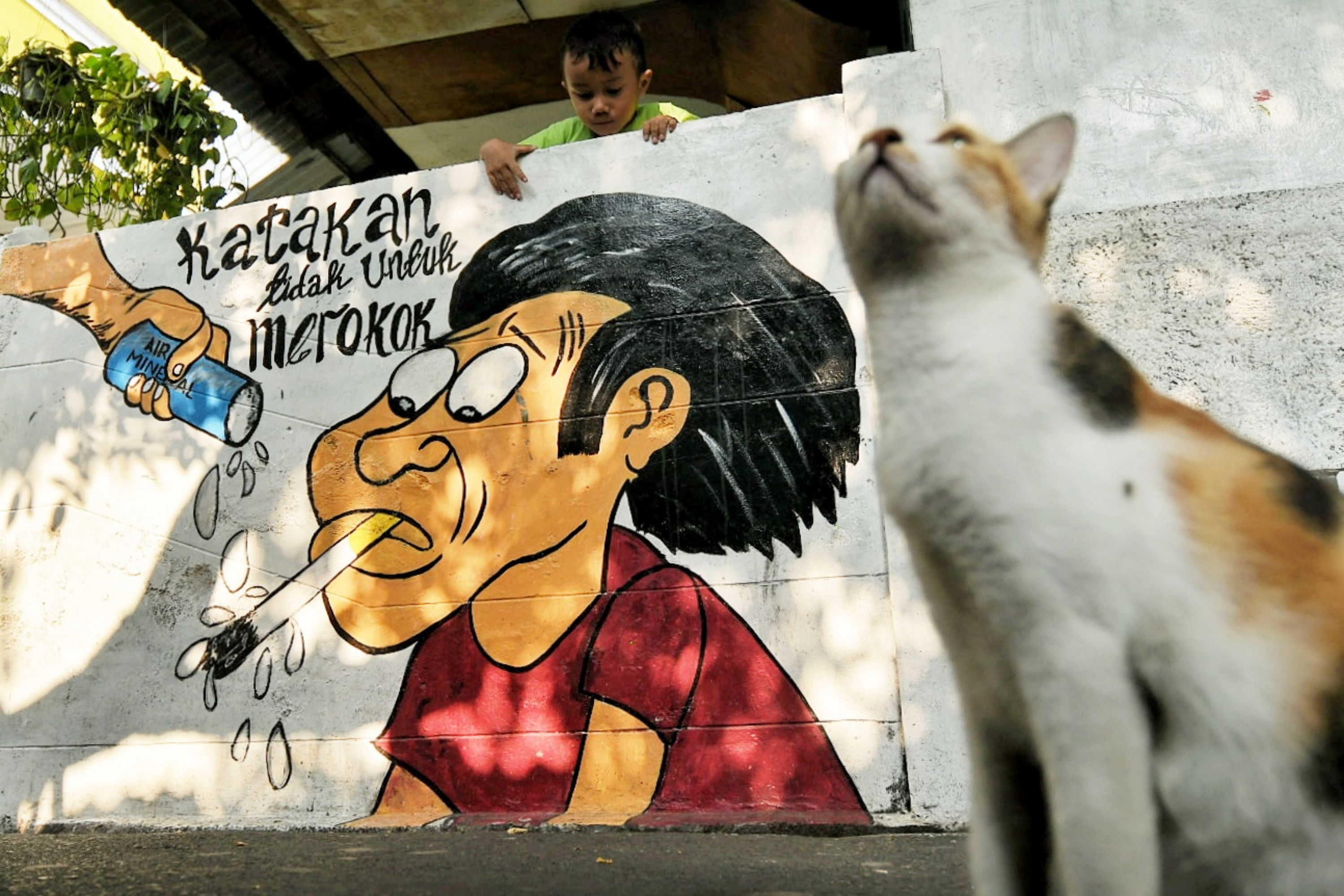 Warga beraktivitas di dekat mural bertema kawasan bebas asap rokok di lingkungan RW 06 Kelurahan Kayu Manis, Matraman, Jakarta.