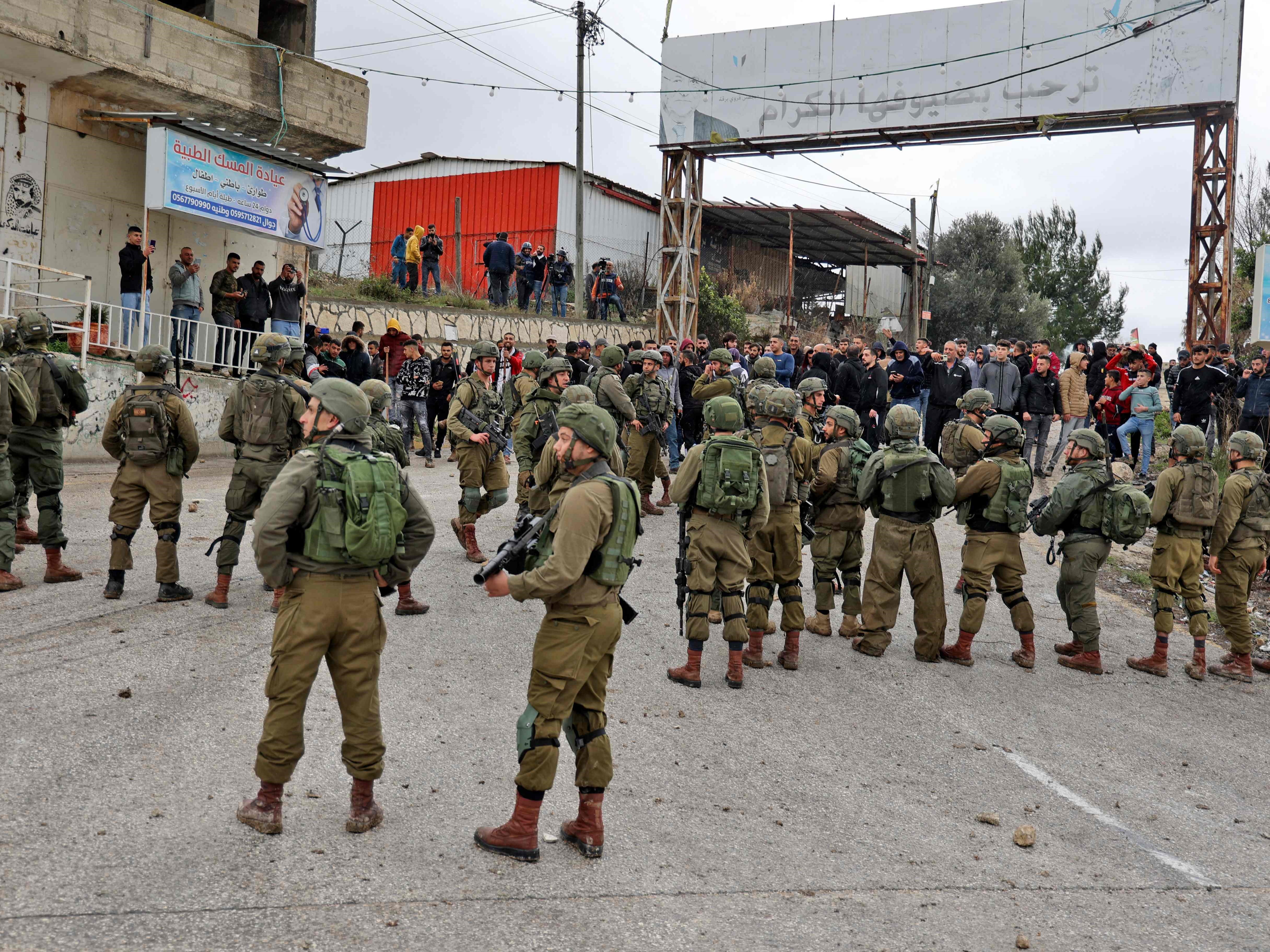 Tentara Israel berdiri di antara pemukim dan penduduk Palestina di desa Burqah, Jumat (17/12), setelah laporan serangan pemukim di desa itu.