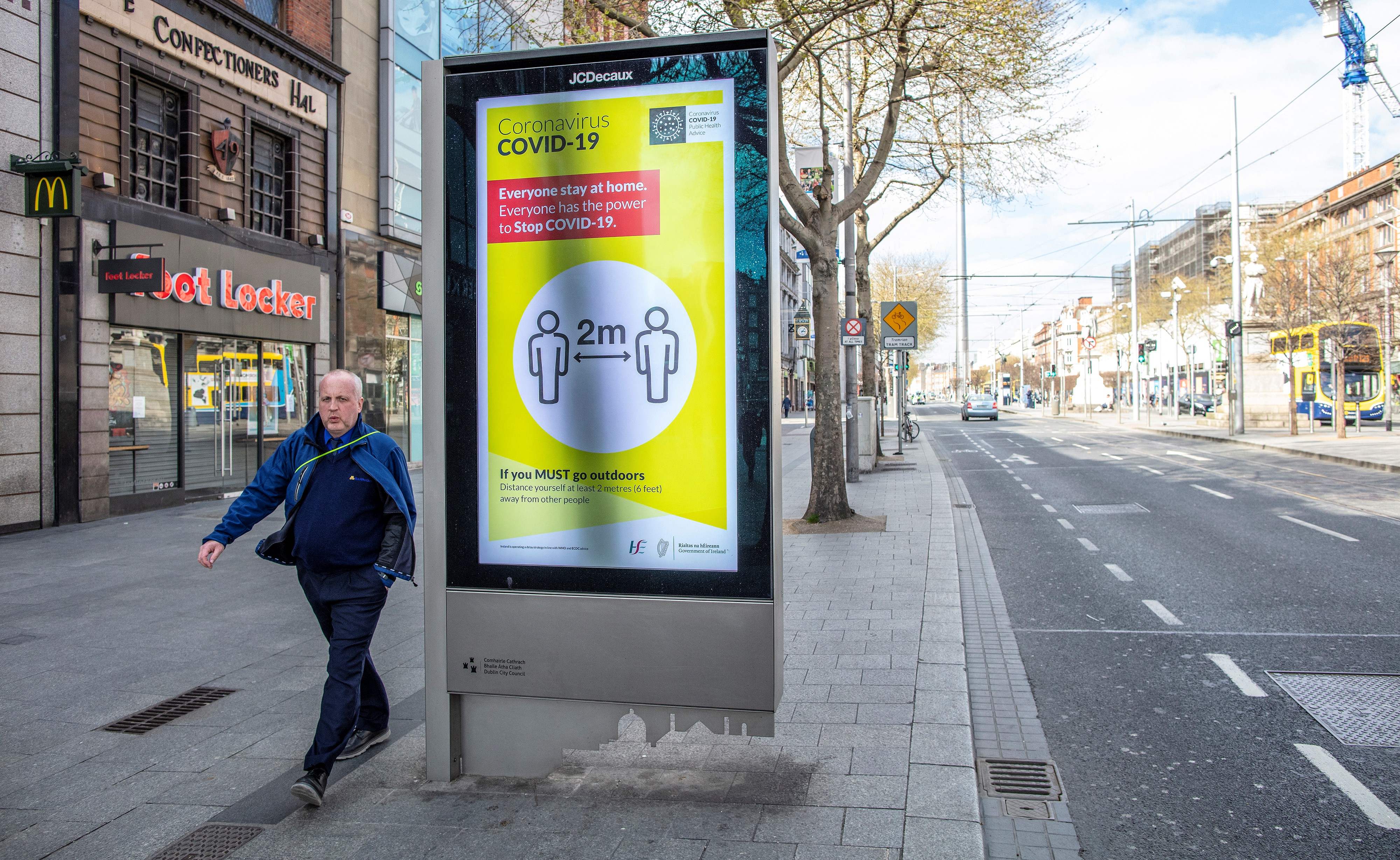 Seorang warga berjalan dengan papan pengumuman untuk menerapkan 'physical distancing' di Kota Dublin, Irlandia. 