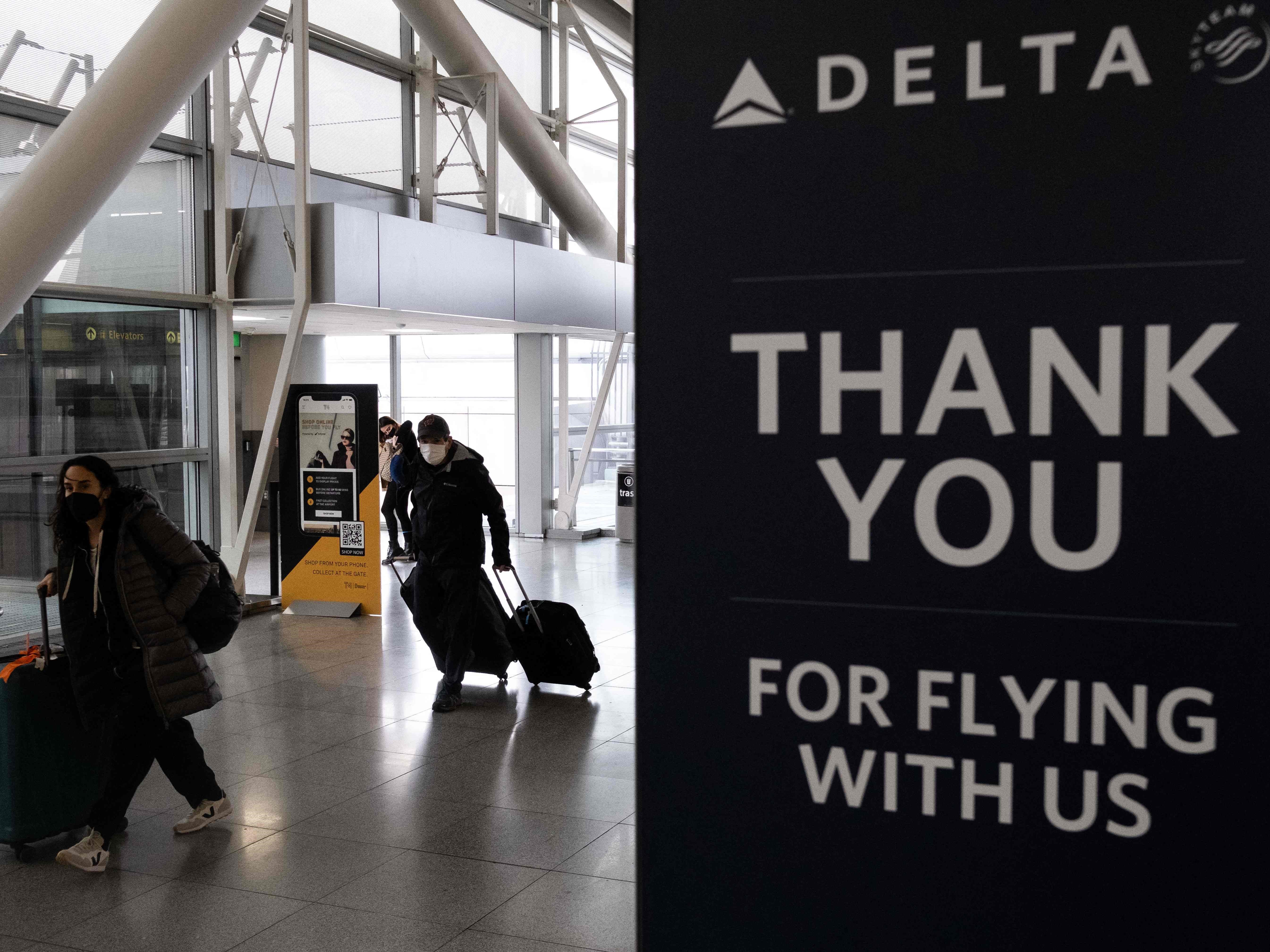 Pelancong yang membawa koper berjalan melewati tanda Delta Airlines di John F. Kennedy International Airport, New York, Jumat (24/12).