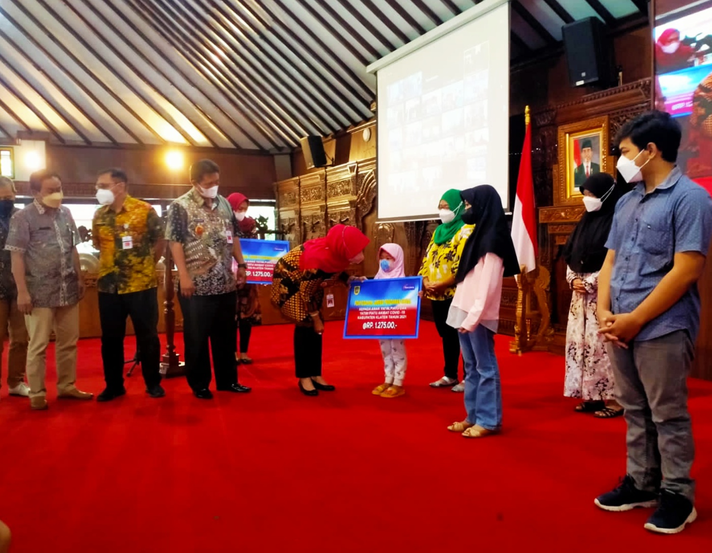 Bupati Sri Mulyani (membungkuk) menyerahkan bantuan sosial kepada seorang anak yang orangtuanya meninggal karena covid-19.