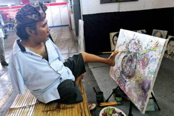 Perupa disabilitas Kadek Windari Karunadhita melukis dengan kakinya. 